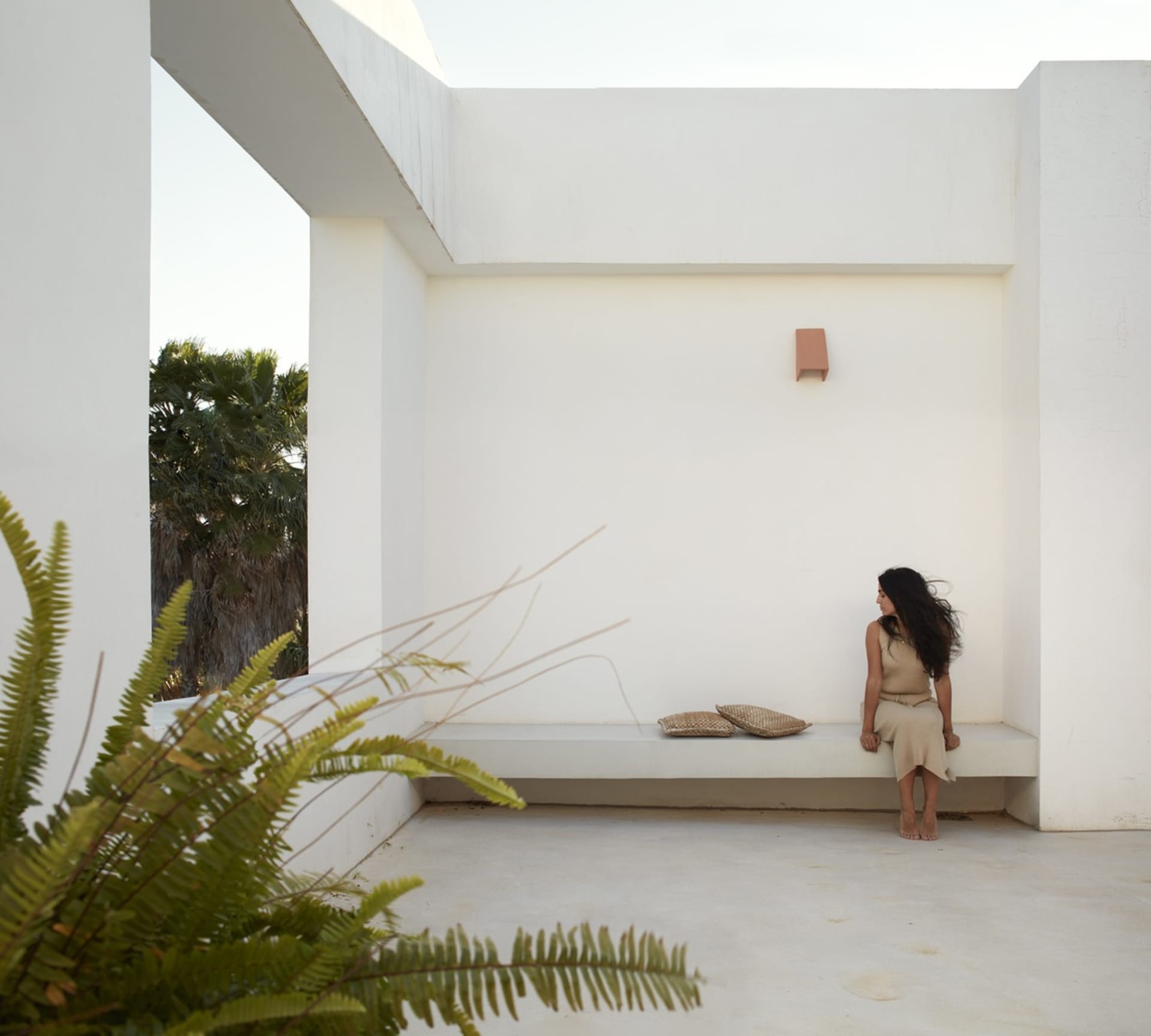 A minimalist outdoor space with clean lines, concrete walls, and a woman sitting on a low wall.