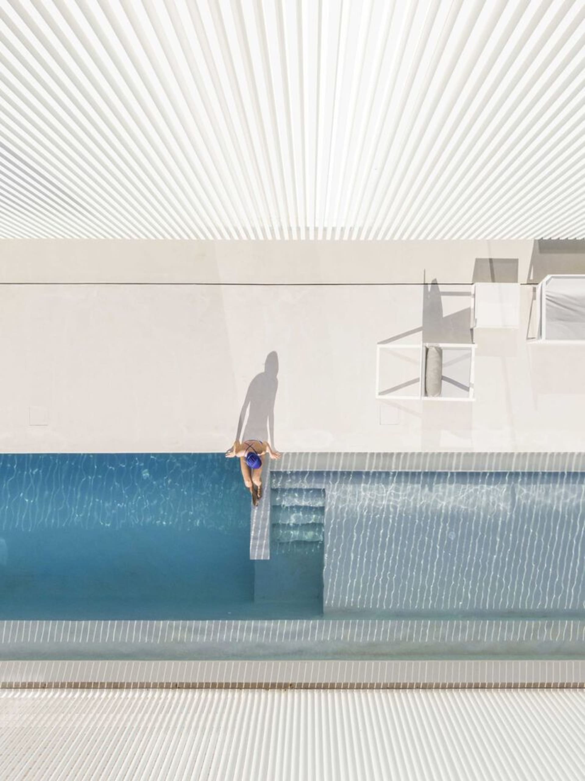 A modern white plaster pool area with a person walking towards the edge.