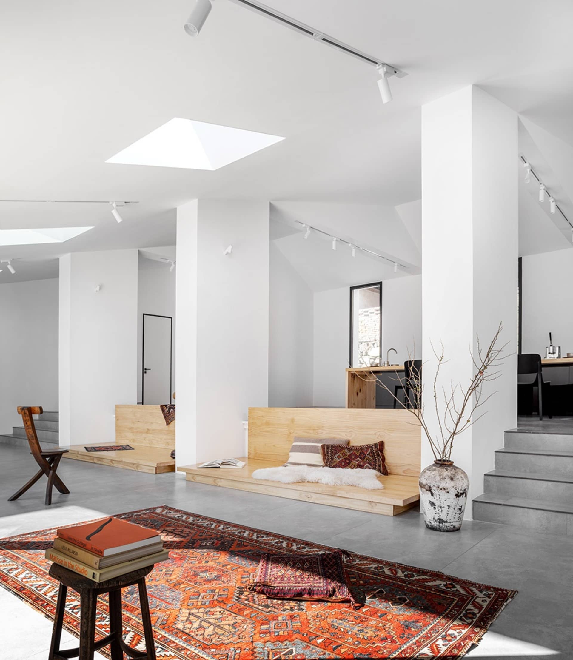 A minimalist living room features wooden benches and a large rug in a modern space.