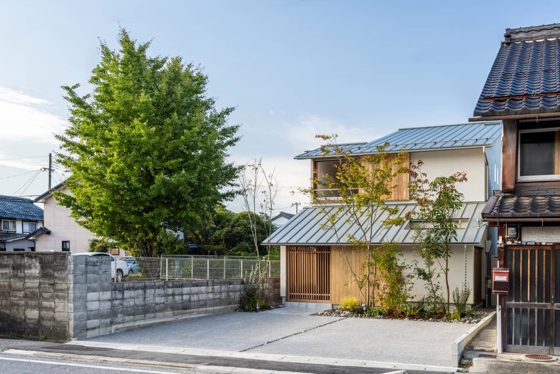 現代住宅外觀,搭配金屬屋頂、木質框架,以及被綠意環繞的混凝土車道。