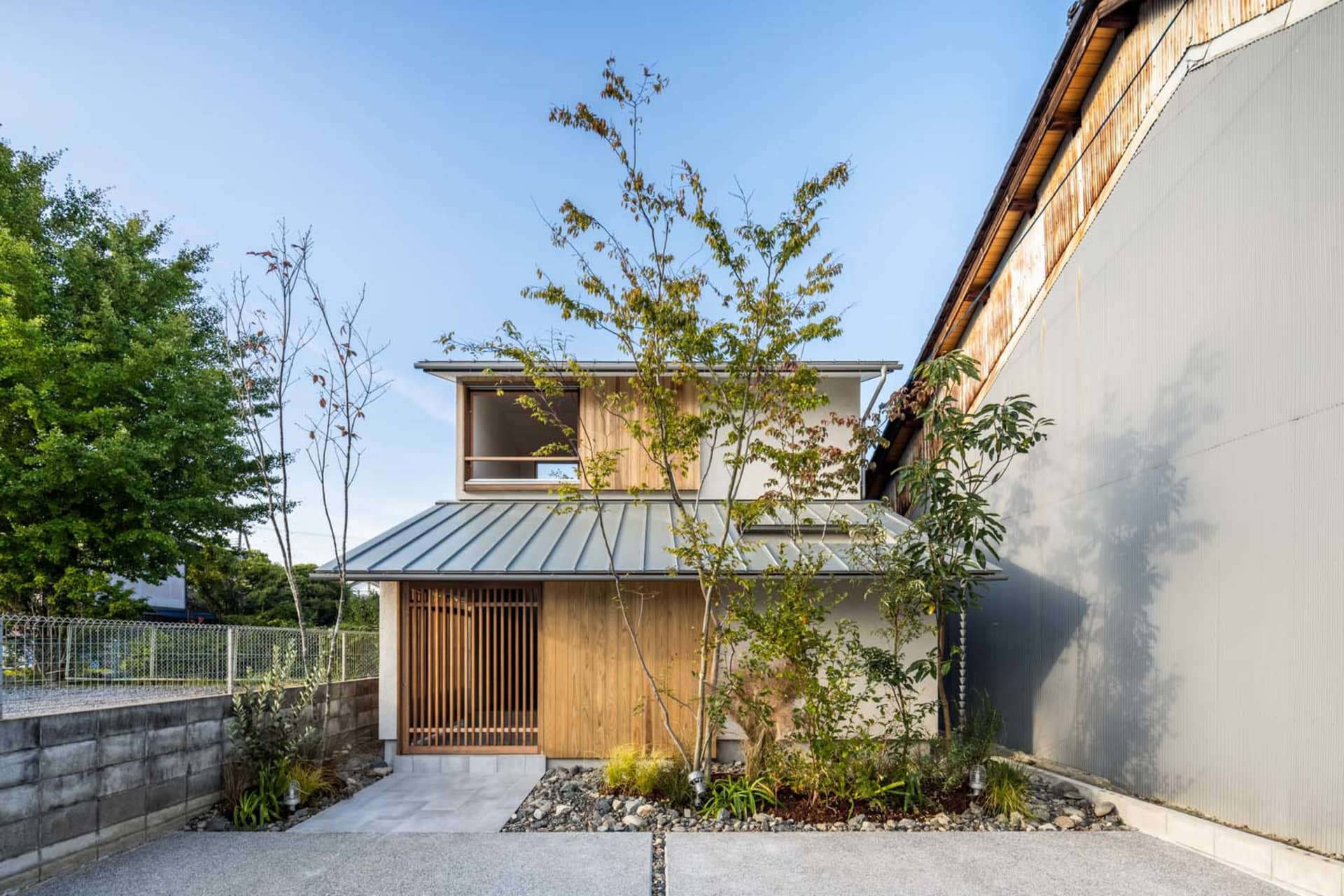 A modern residential exterior with a metal roof and wooden structure, featuring a minimalist design and a small garden with t