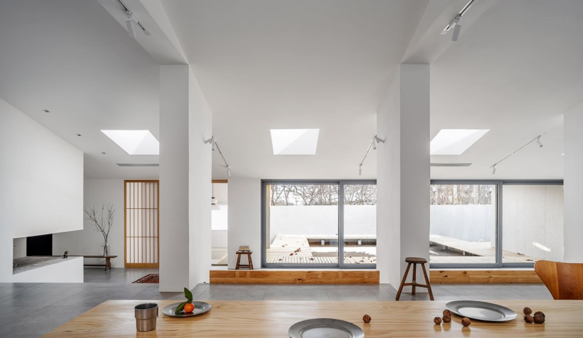Modern minimalist living room featuring concrete floors, wooden furnishings, and large glass windows.