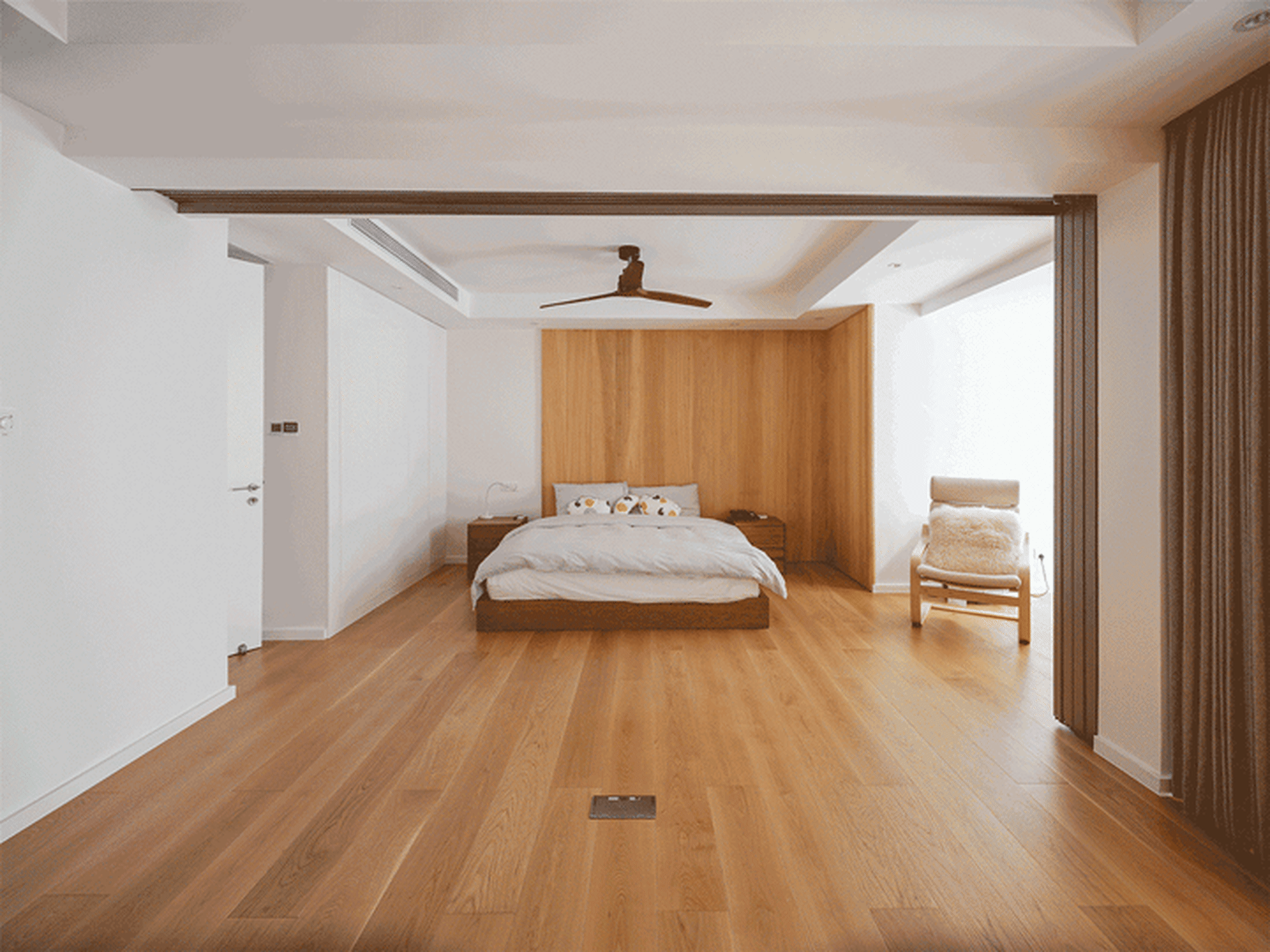 A minimalist bedroom featuring a wooden floor, white furniture, and a wooden headboard.