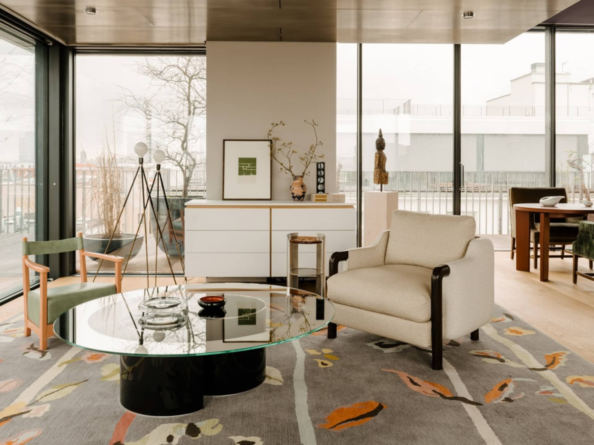Modern living room with glass coffee table, wooden armchair, and colorful carpet