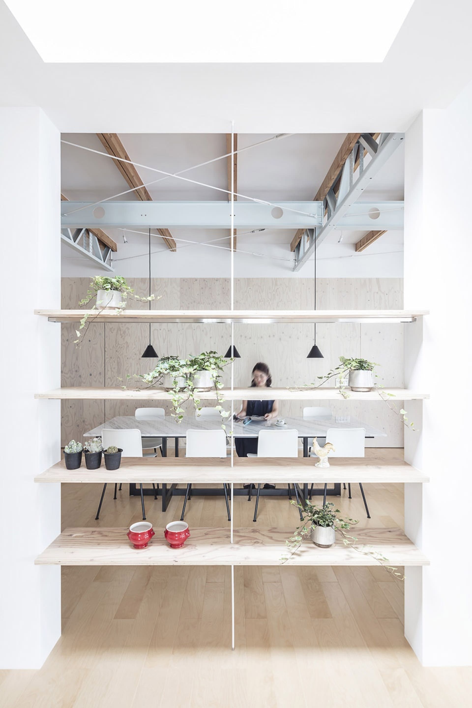 A modern office space with wooden shelves, metal beams, glass walls, and green plants.