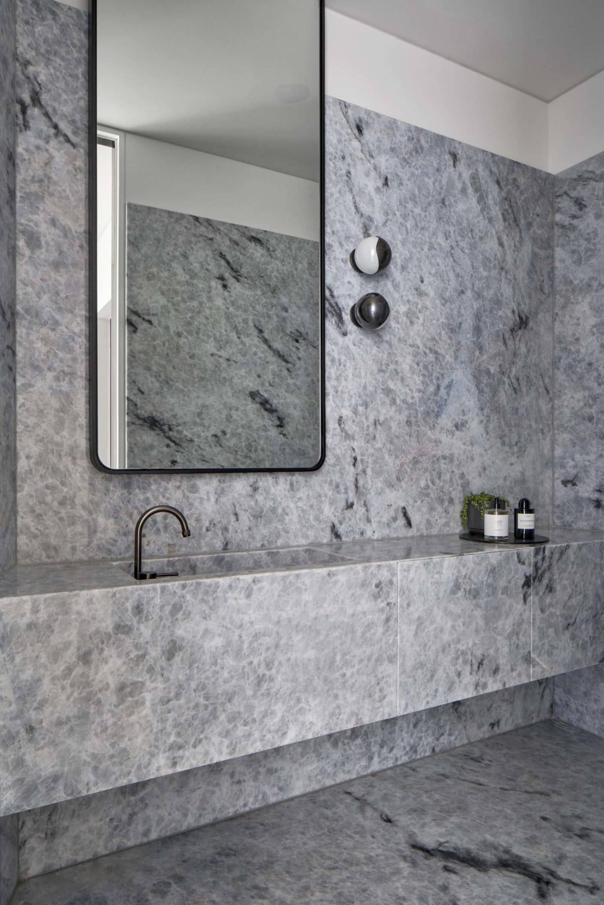 A modern bathroom with marble walls and floor, featuring a floating vanity with a black faucet and a large rectangular mirror