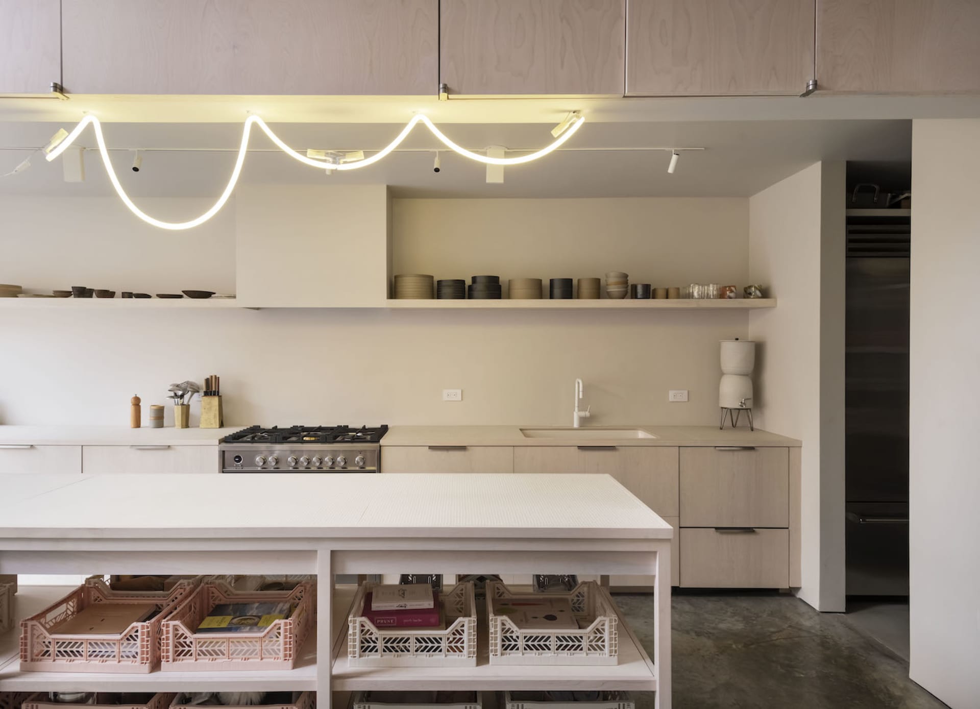 A modern minimalist kitchen with clean lines, light wood cabinets, and a white island.