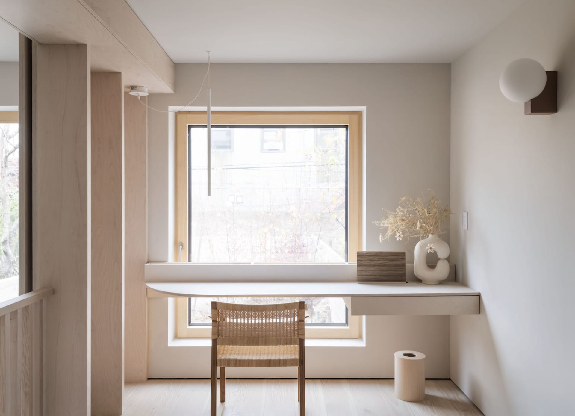 A minimalist home office with a small white desk, wooden chair, and a vase of flowers.