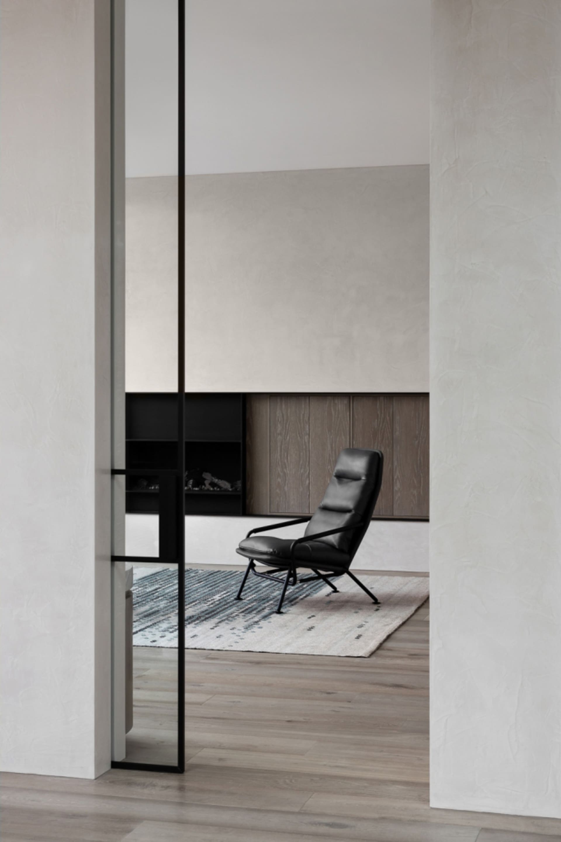 A modern living room features a black leather chair on a textured rug.