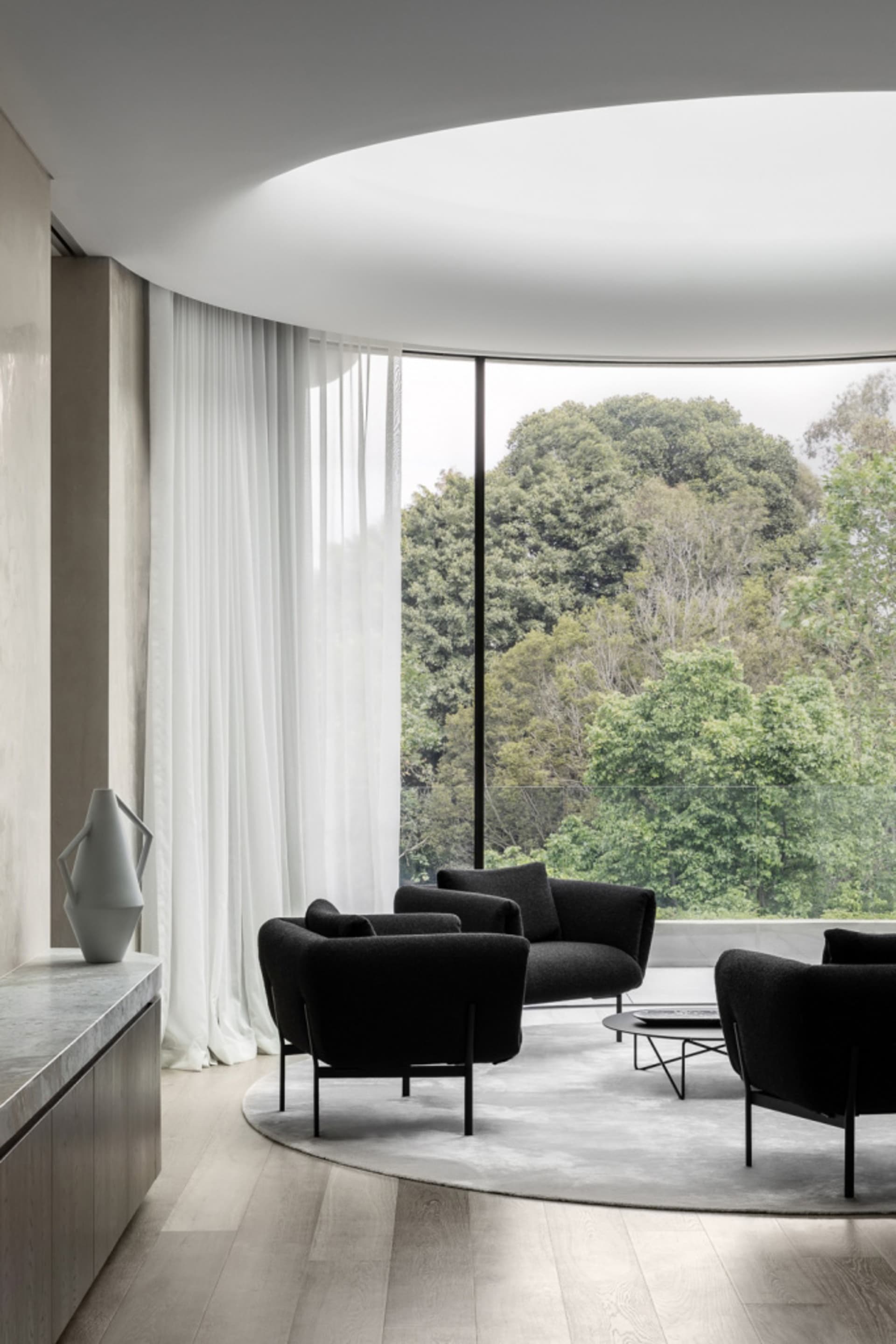 Modern living room featuring black upholstered chairs and a round coffee table with a minimalist design, set against a backdr