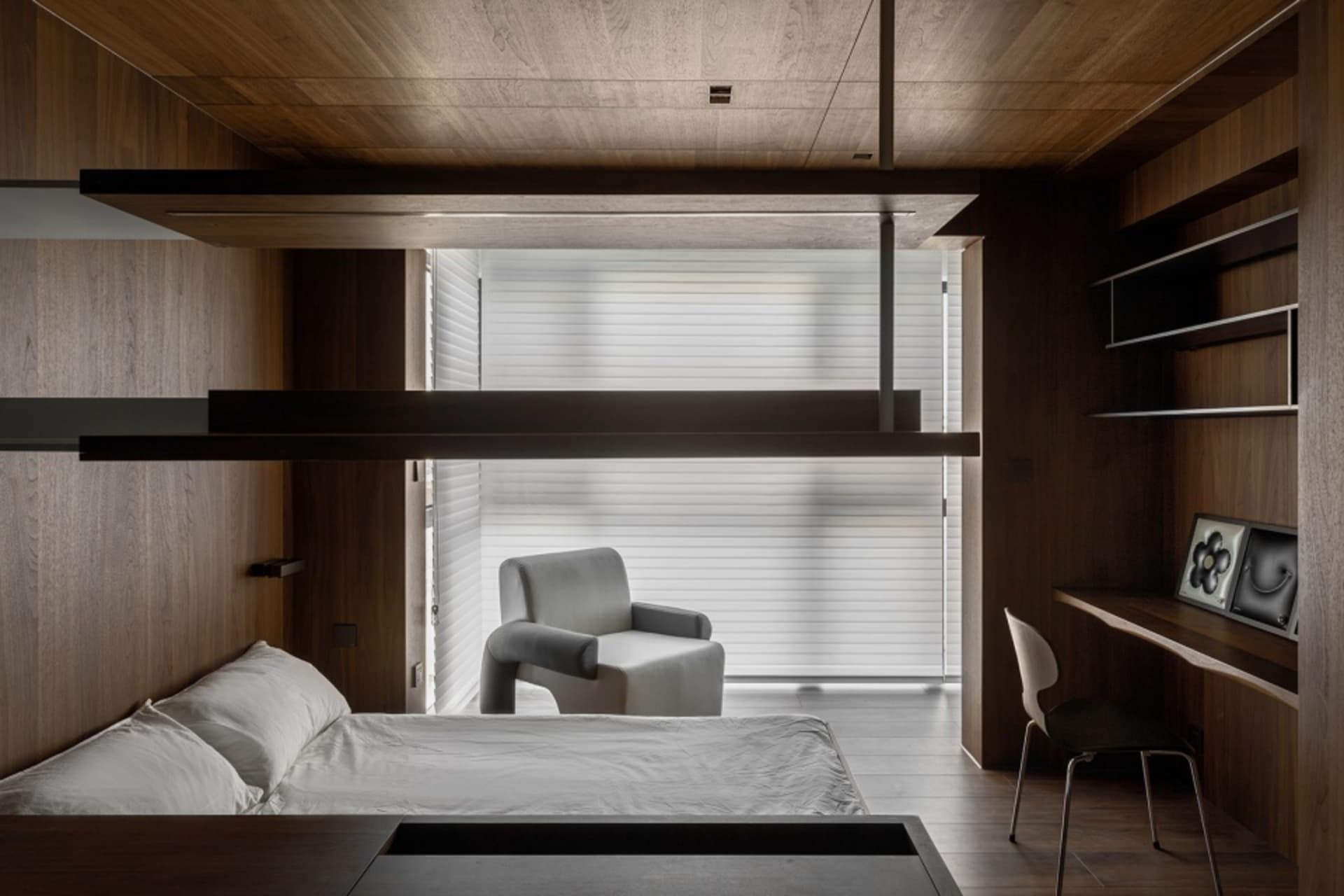 A modern bedroom featuring wooden furniture, a white armchair, and a desk with a computer monitor.