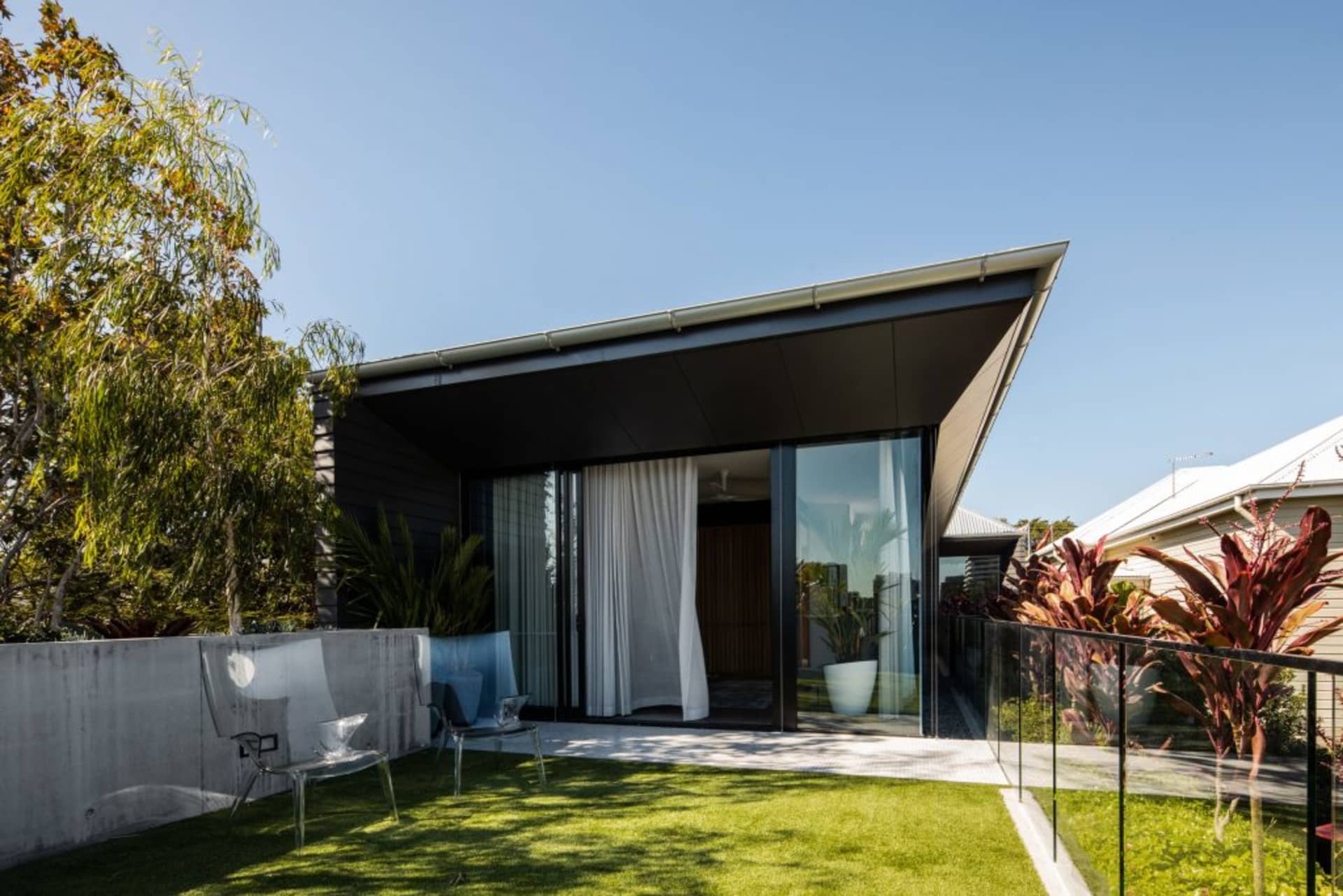 A modern house exterior featuring glass walls, concrete patio, and surrounding greenery.