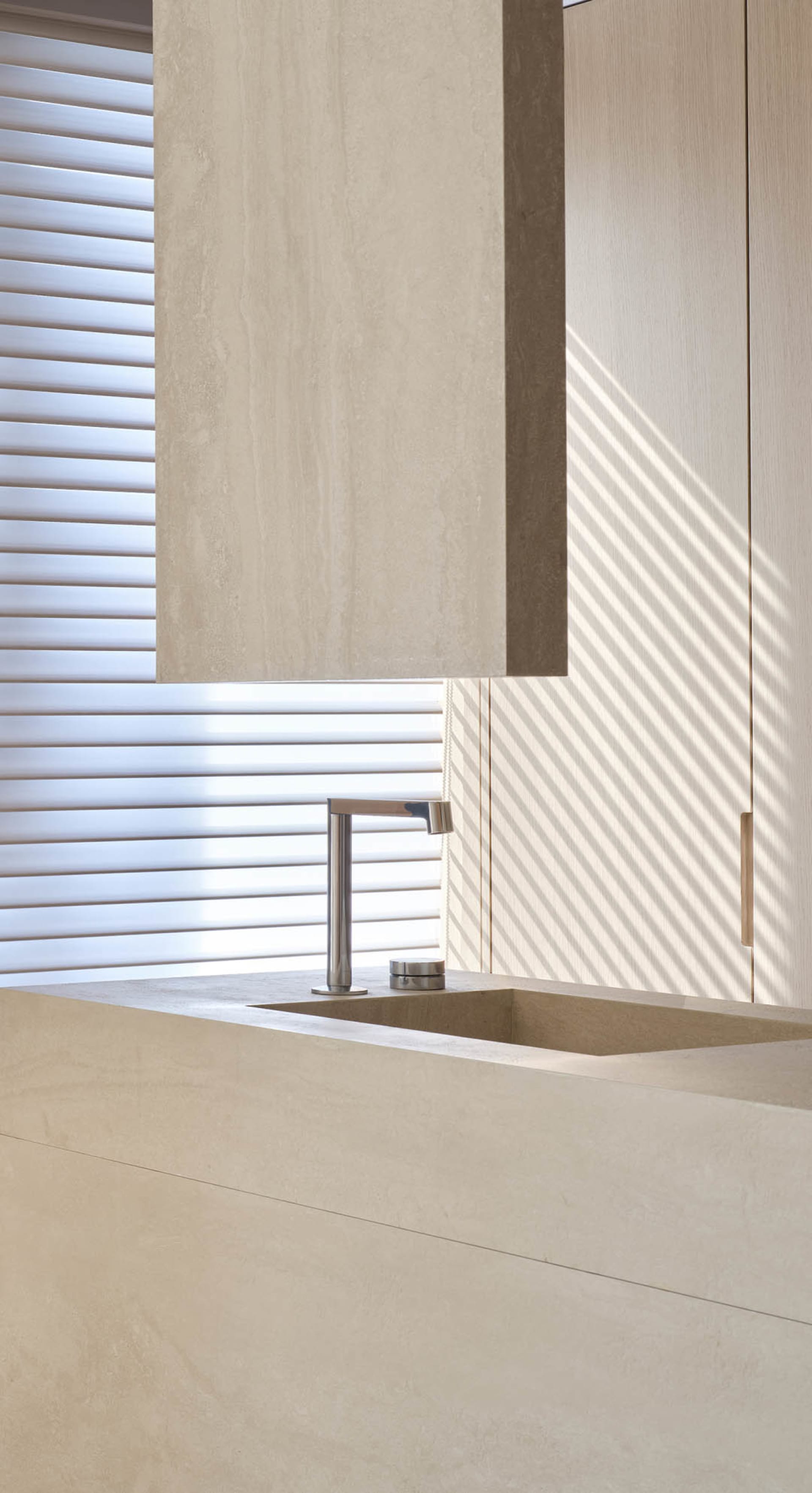 A minimalist bathroom featuring a concrete sink, modern faucet, and light streaming through a window with vertical blinds.