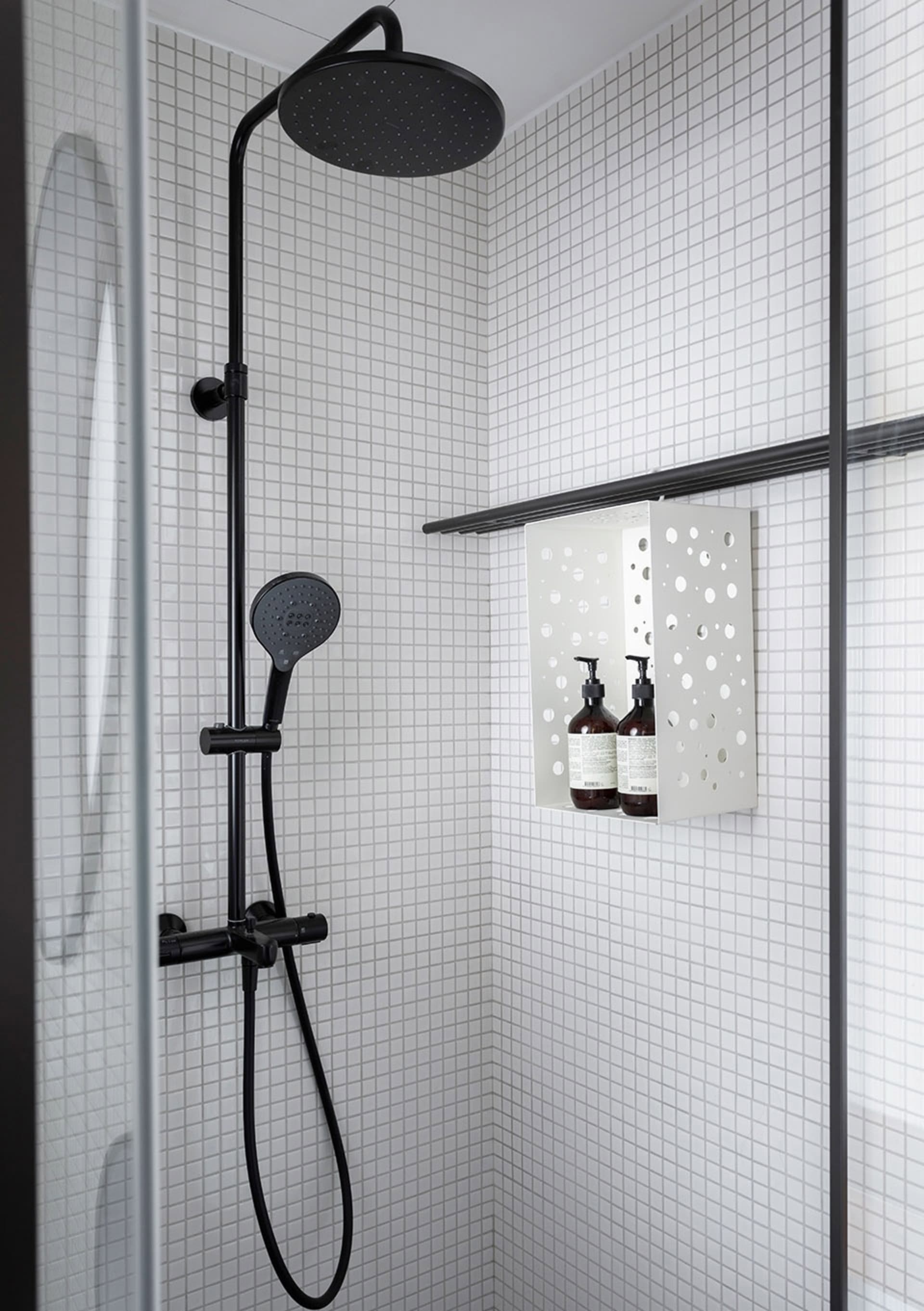 A minimalist bathroom featuring a shower with black fixtures and white square tiles on the walls.