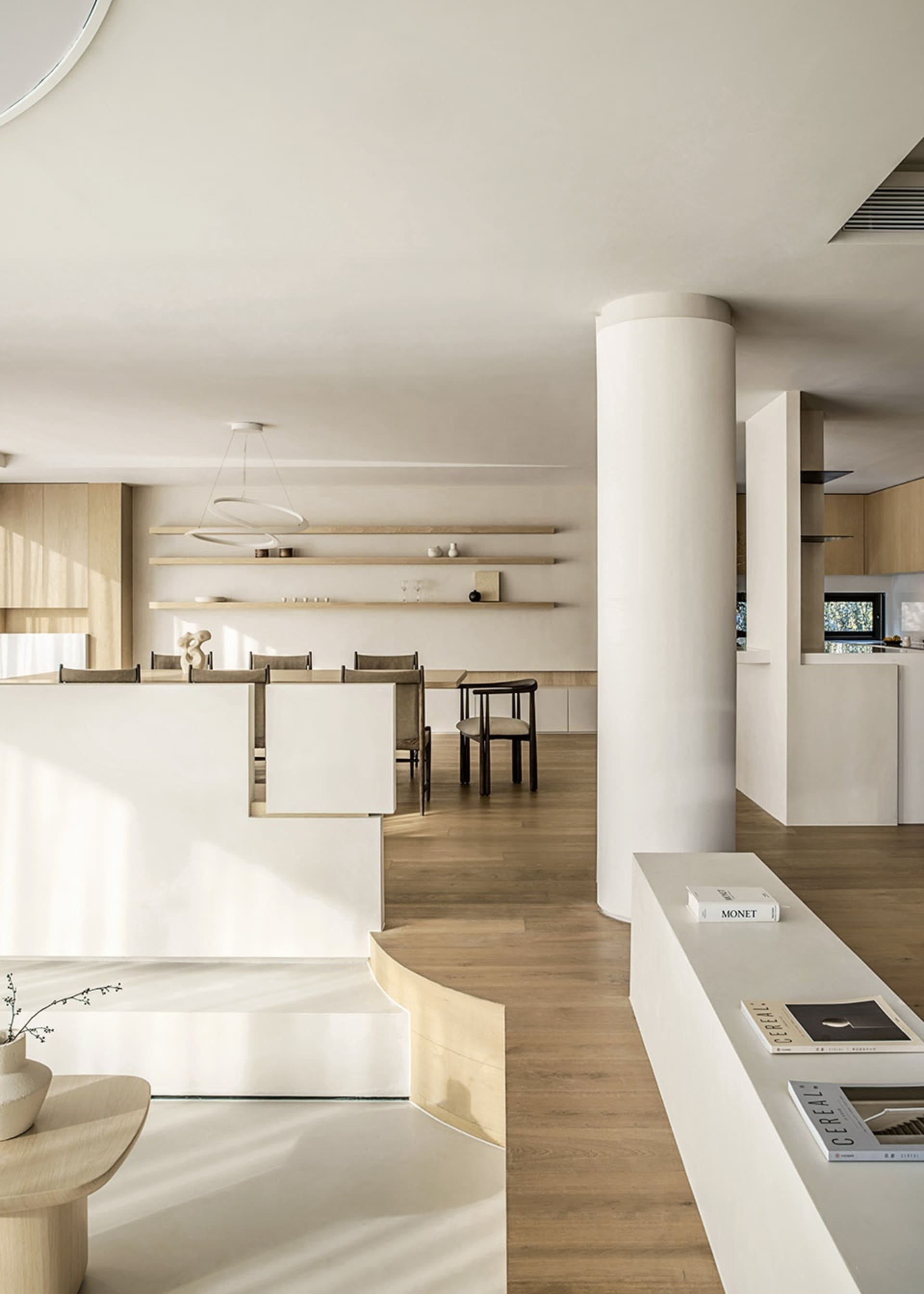 A modern minimalist kitchen and living space featuring white walls, wooden furniture, and open shelving.