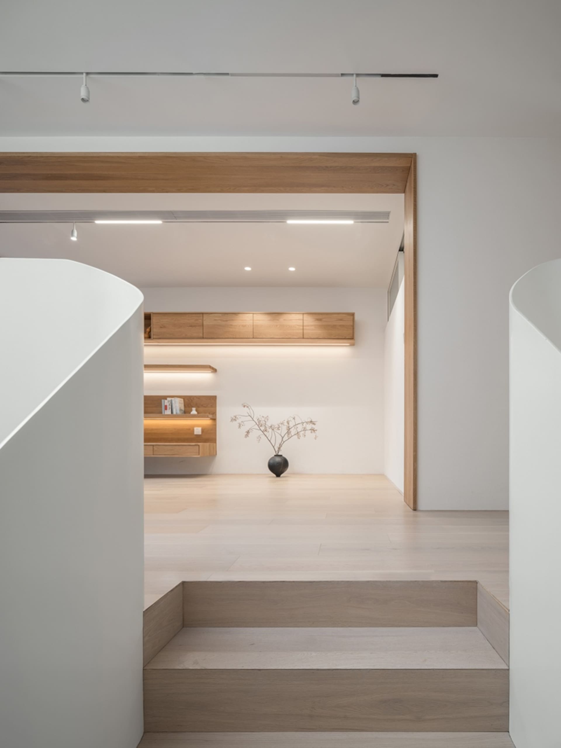 A minimalist living room with wooden elements and a vase with branches on the floor.
