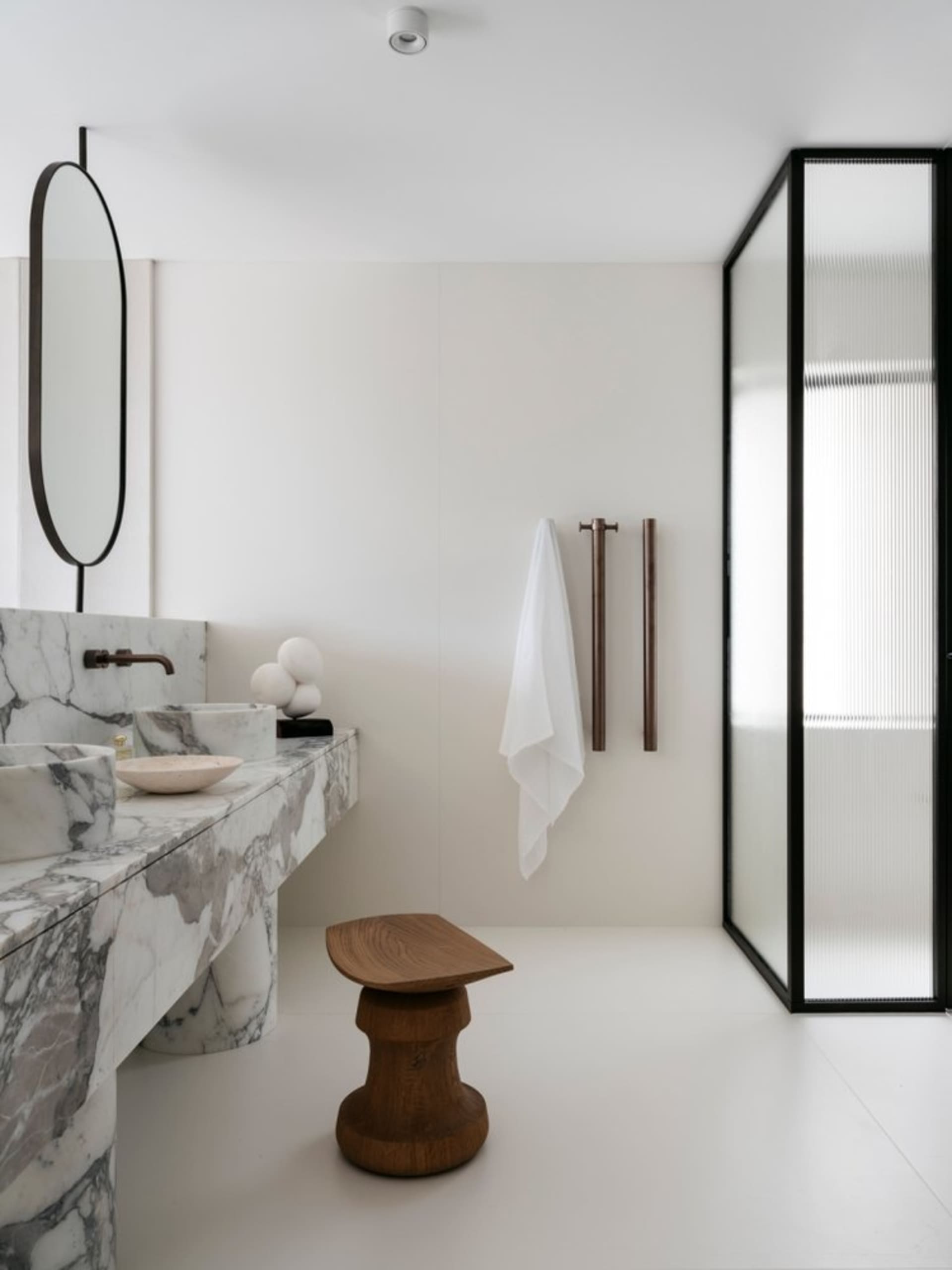 Modern minimalist bathroom with marble sink and floor, and a wooden stool.