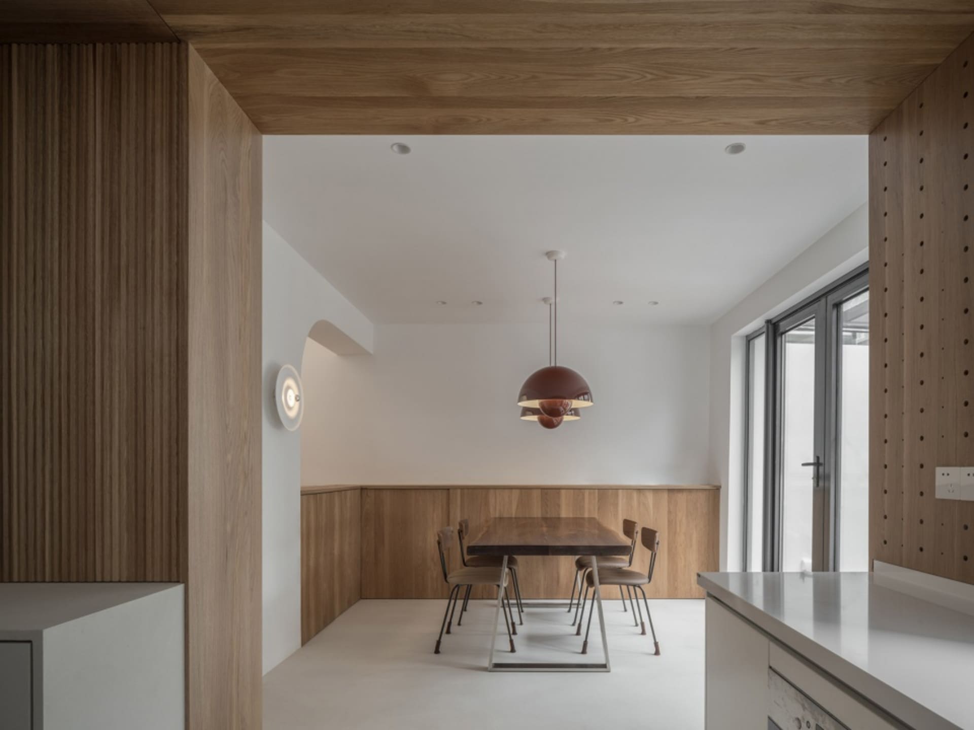 A modern minimalist dining room with wooden furniture, white walls, and a hanging light fixture.