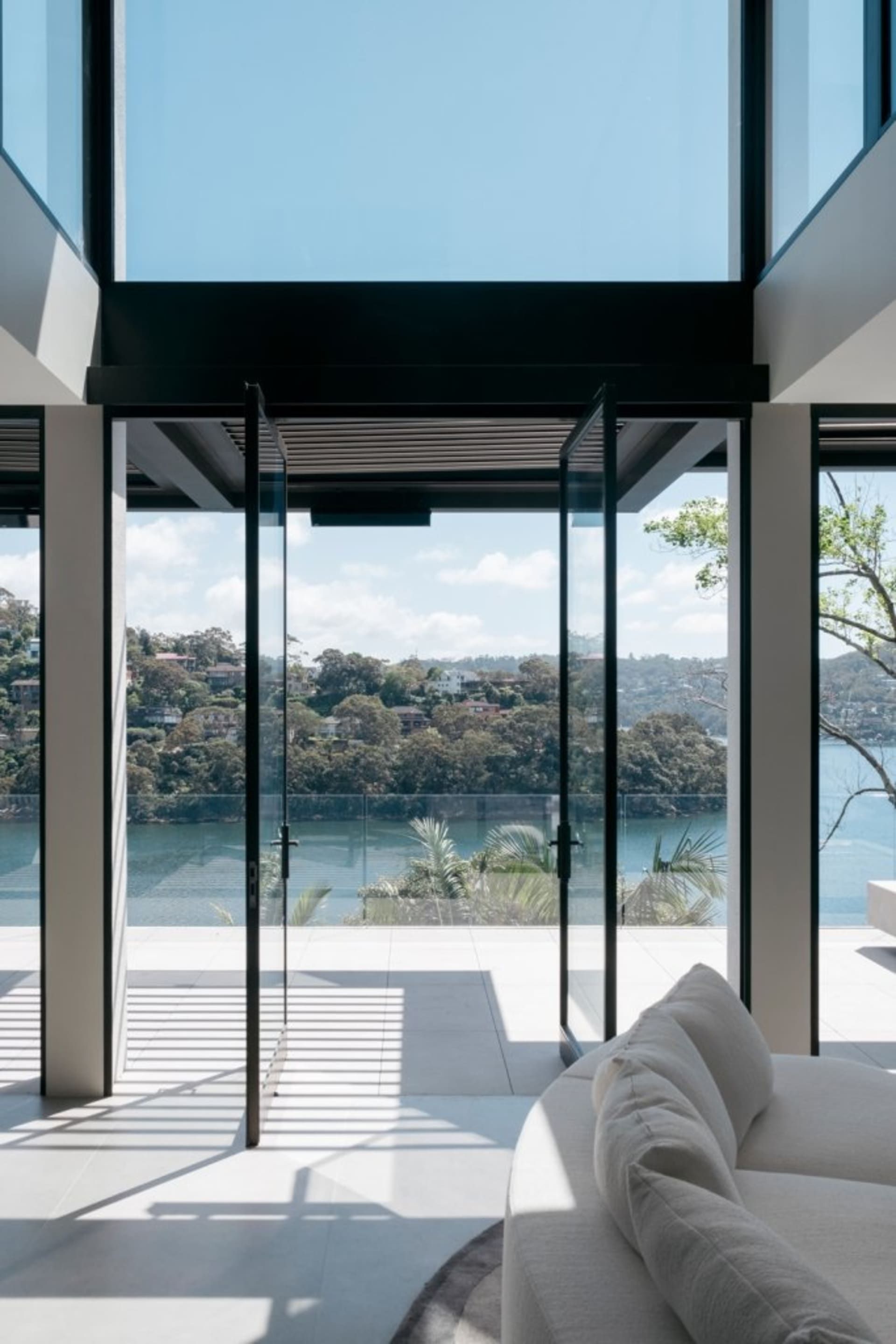 Modern sitting room with large glass wall overlooking a scenic view of water and trees.