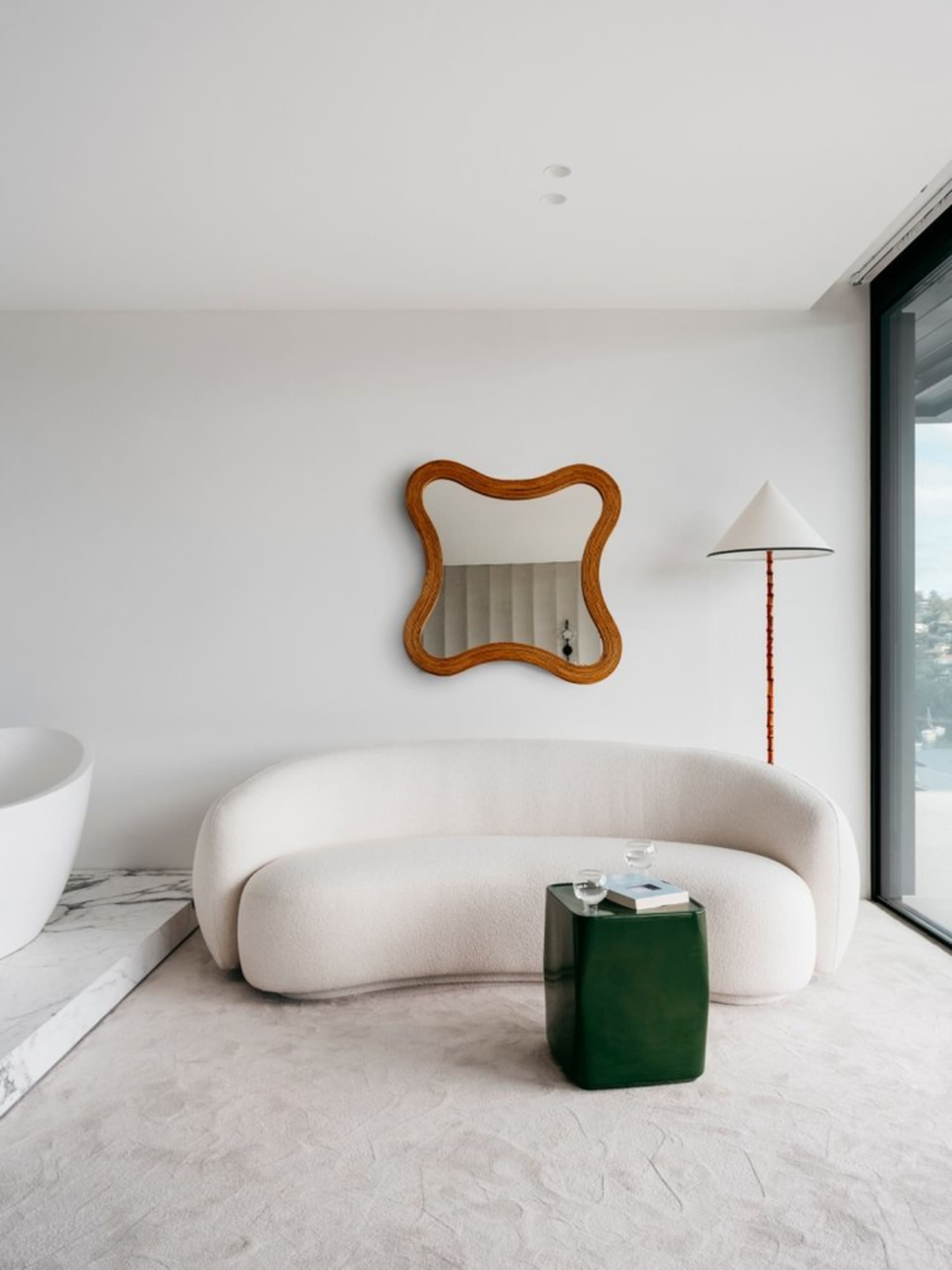 Modern living room featuring a sleek, curved sofa upholstered in a light beige fabric, a white marble floor, and a green meta