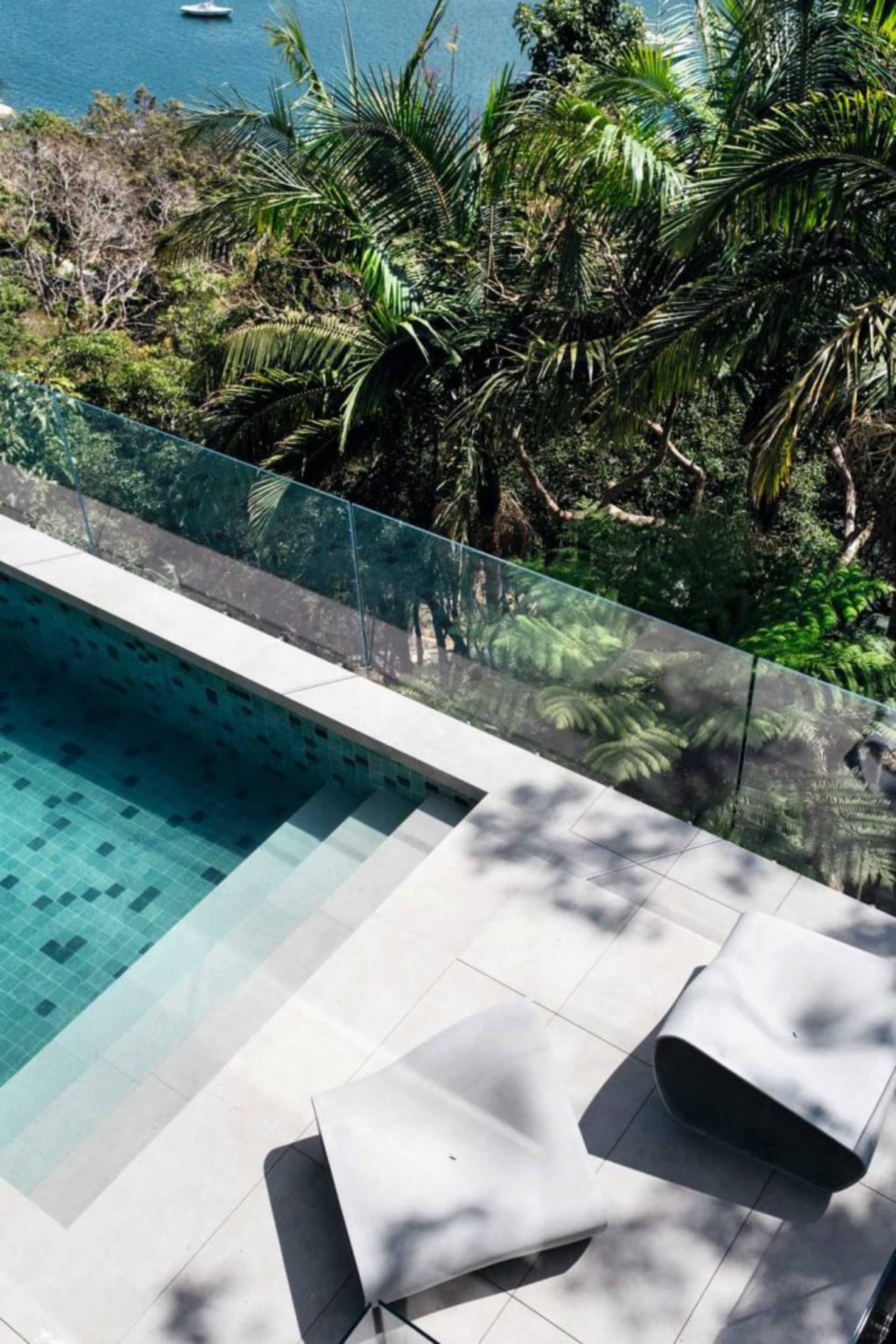 Modern pool deck featuring a glass barrier overlooking a lush tropical landscape.