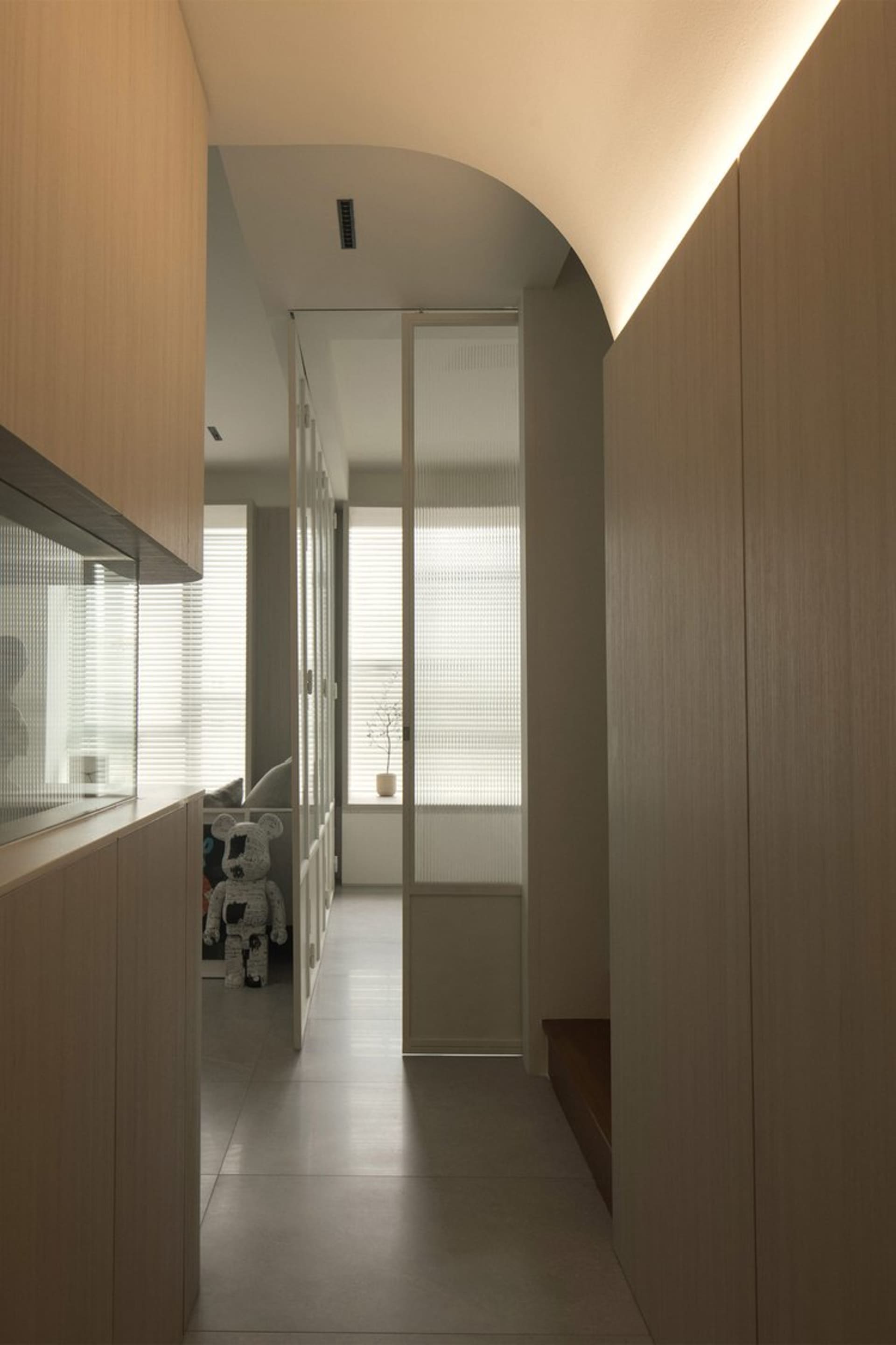 A minimalist residential corridor with wooden cabinets and a light fixture.
