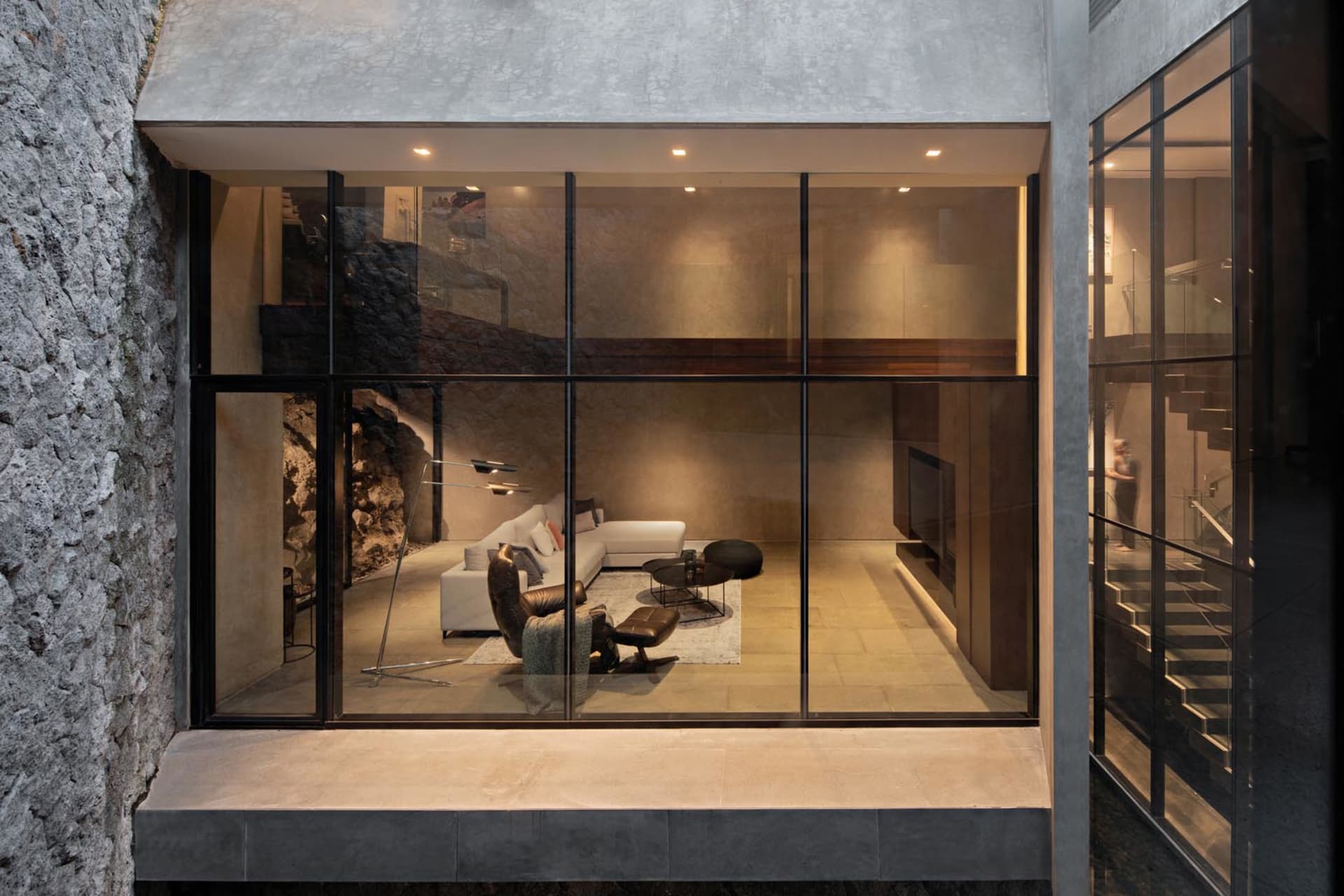 Contemporary living room with concrete walls and floor, featuring minimalist furniture and a cozy atmosphere.