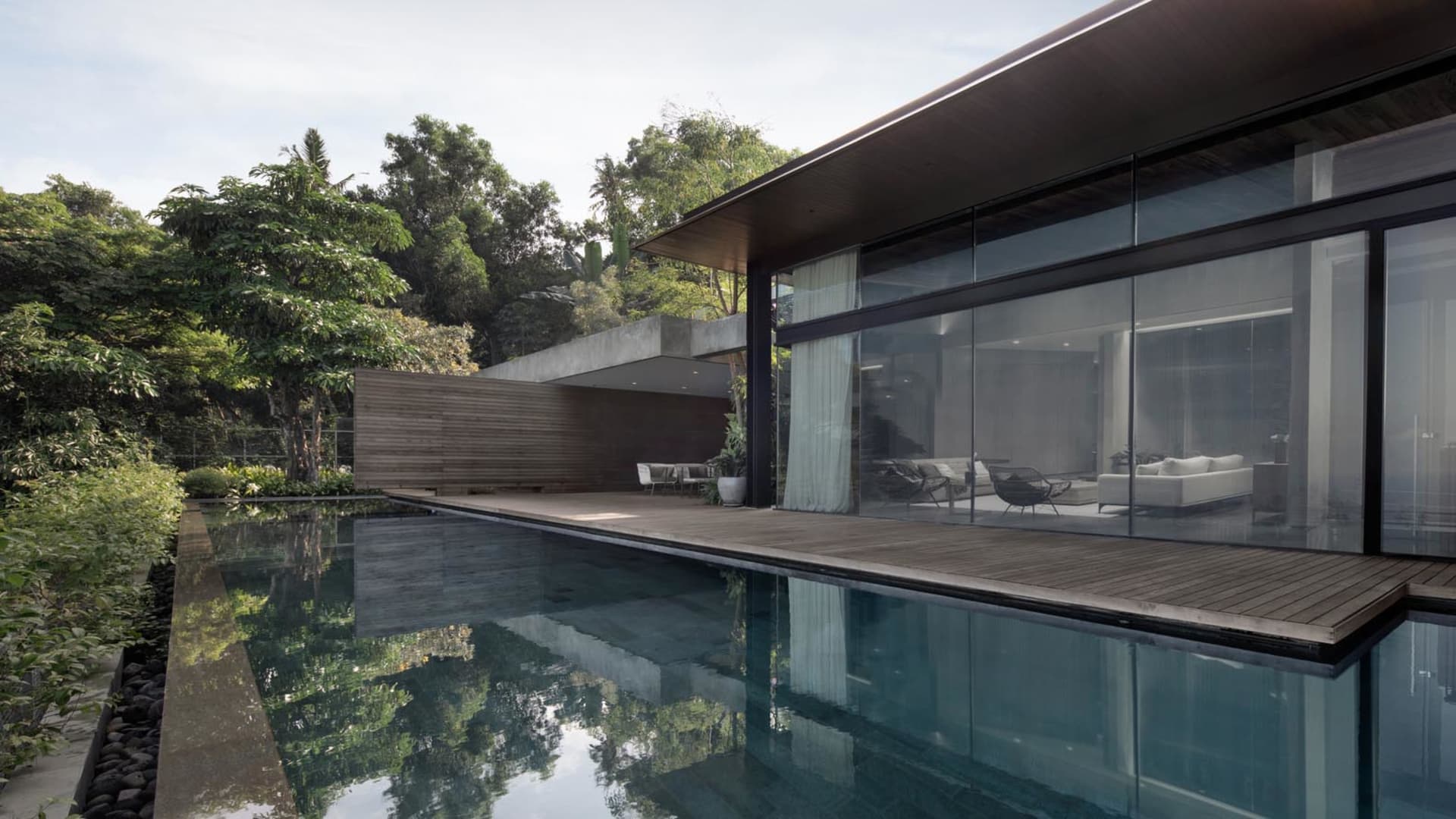 Modern residential exterior featuring glass and wood materials, with a pool in front of the house.