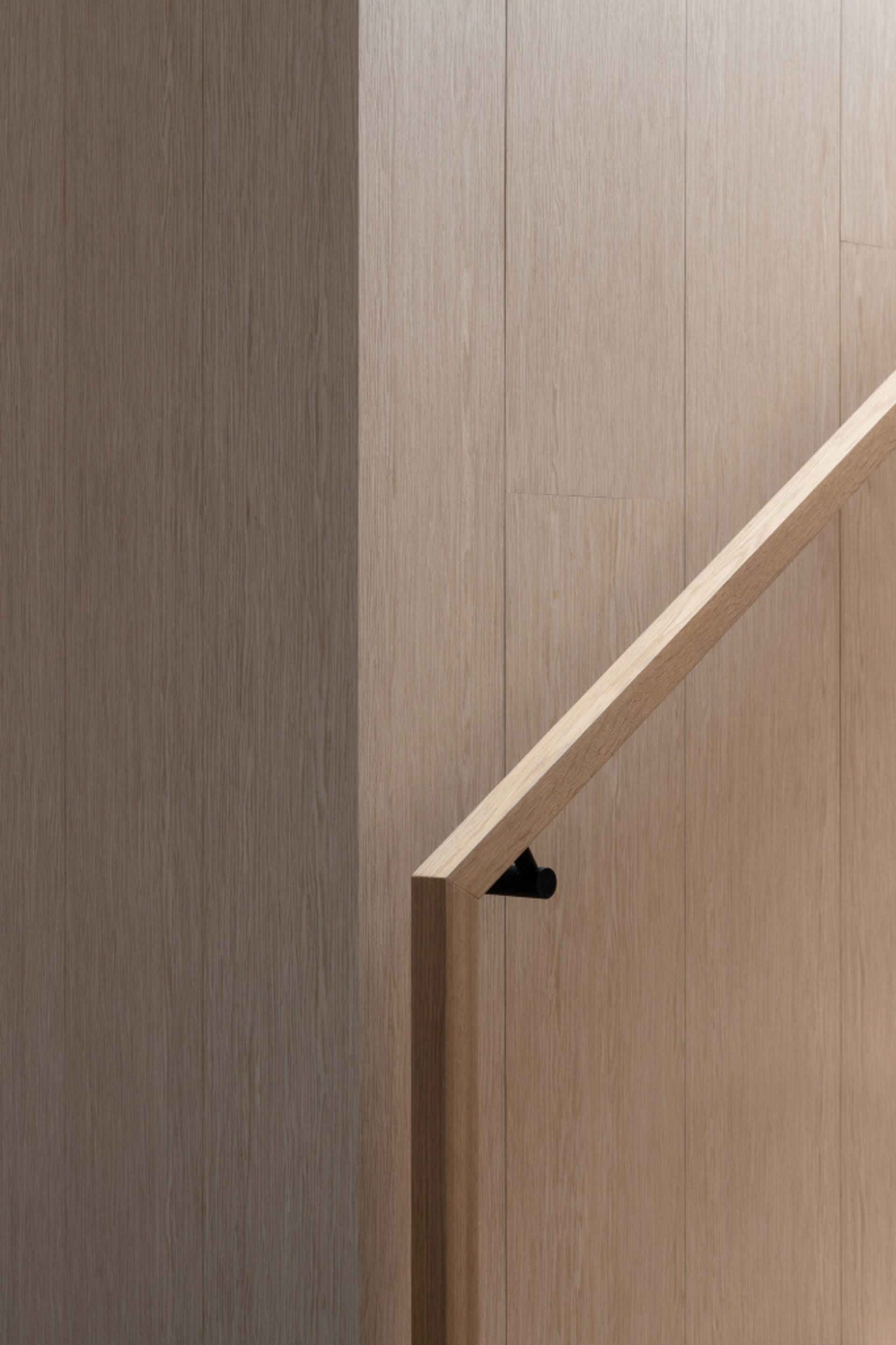 Modern, minimalist wood stair railing with a sleek, horizontal design against a light wooden wall.
