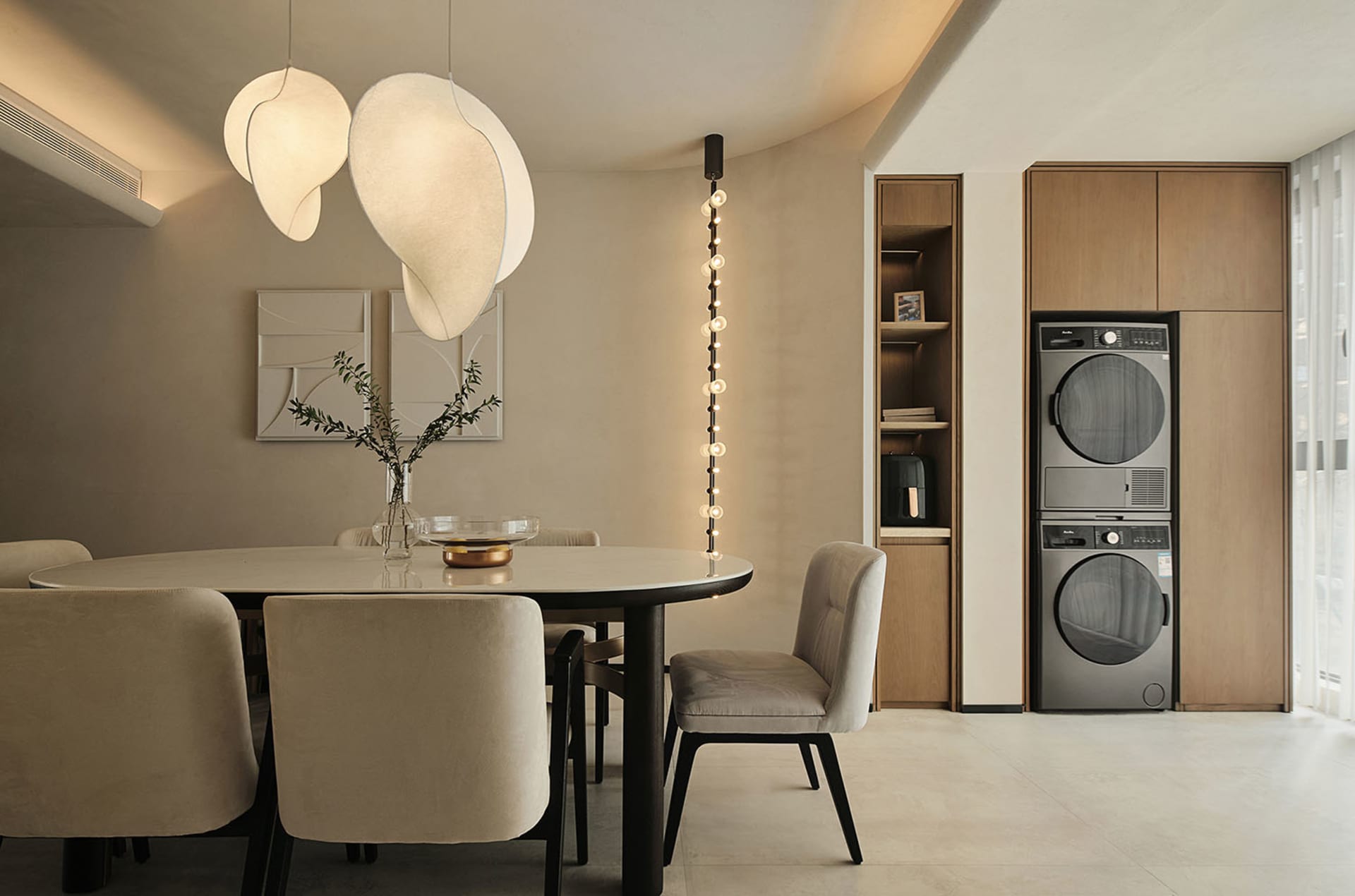 A modern minimalist dining room with a round table, white pendant lights, and wooden cabinets.