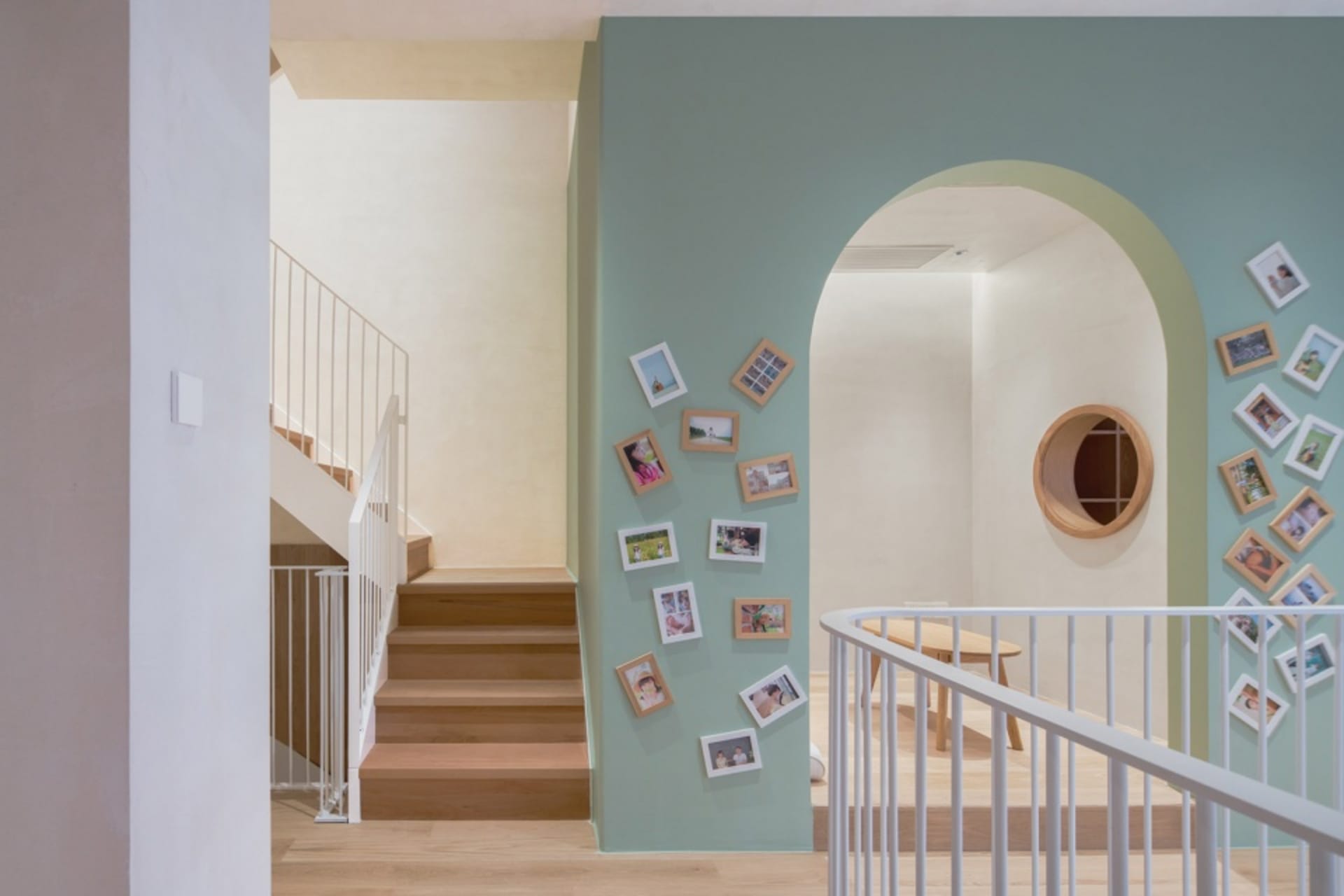 A wooden staircase with a railing, framed photos on the wall, and a table with chairs.