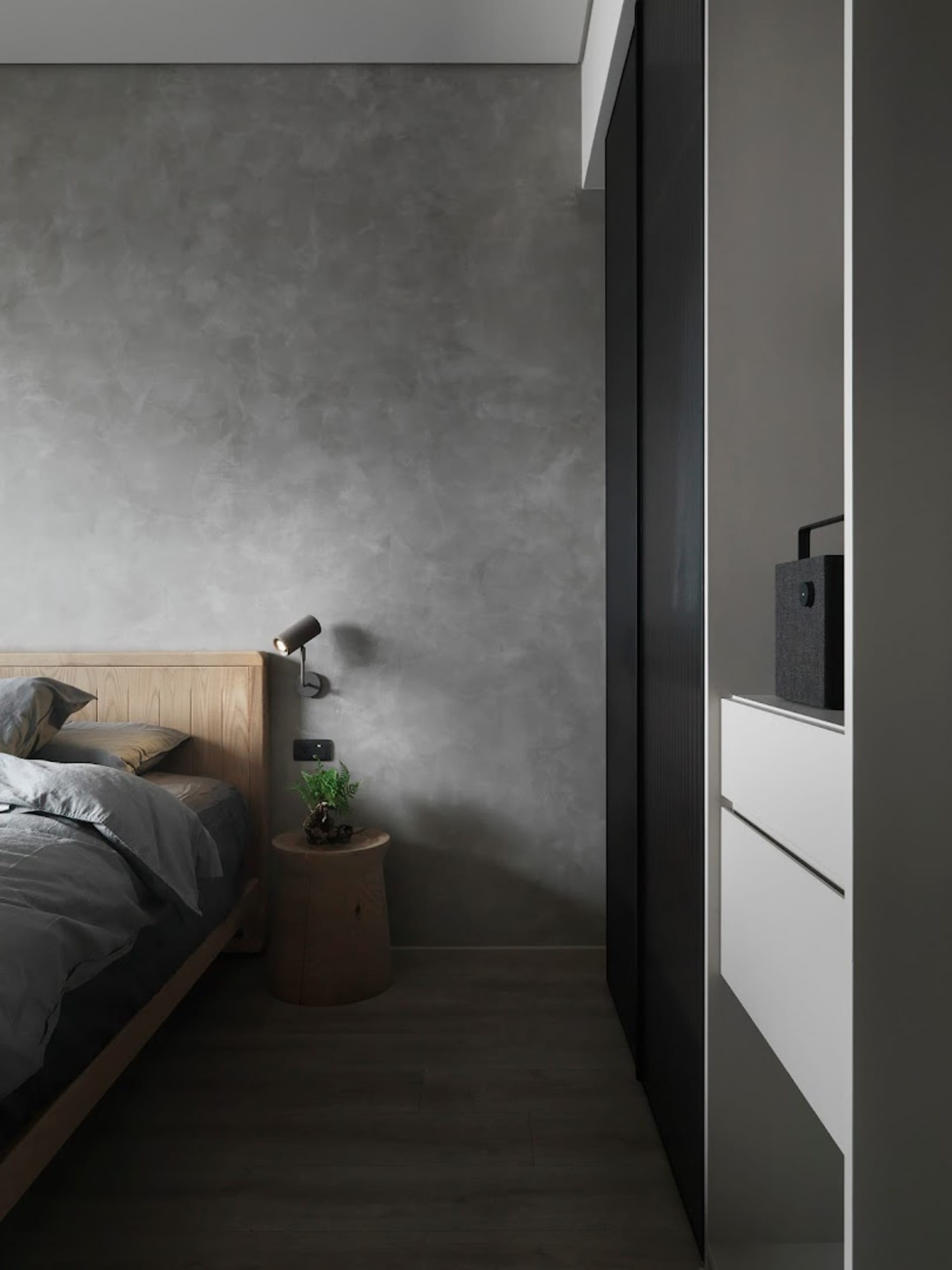 A minimalist bedroom with concrete walls and wooden furniture.