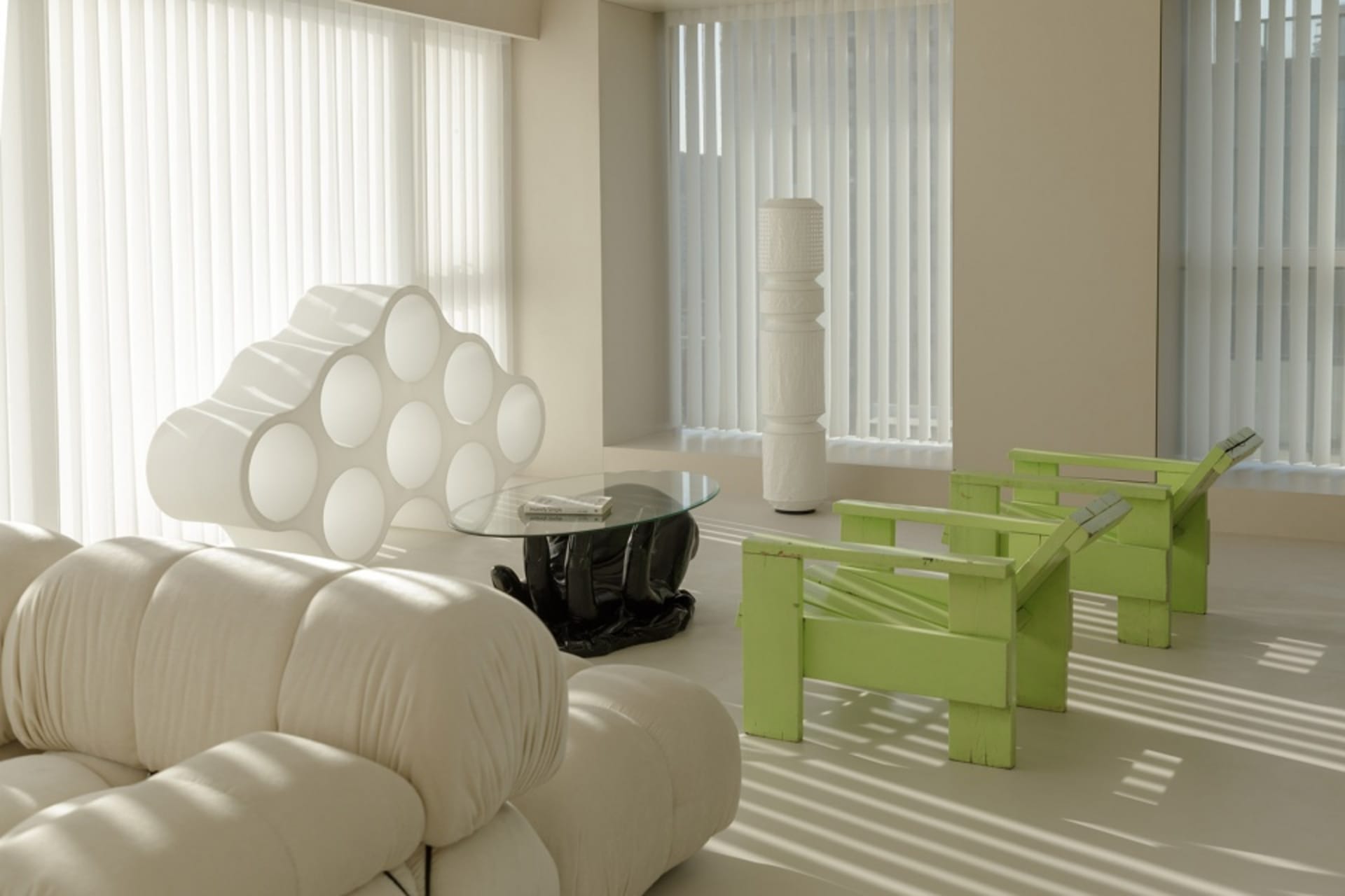 A minimalist living room with white furniture, green chairs, and a glass coffee table.