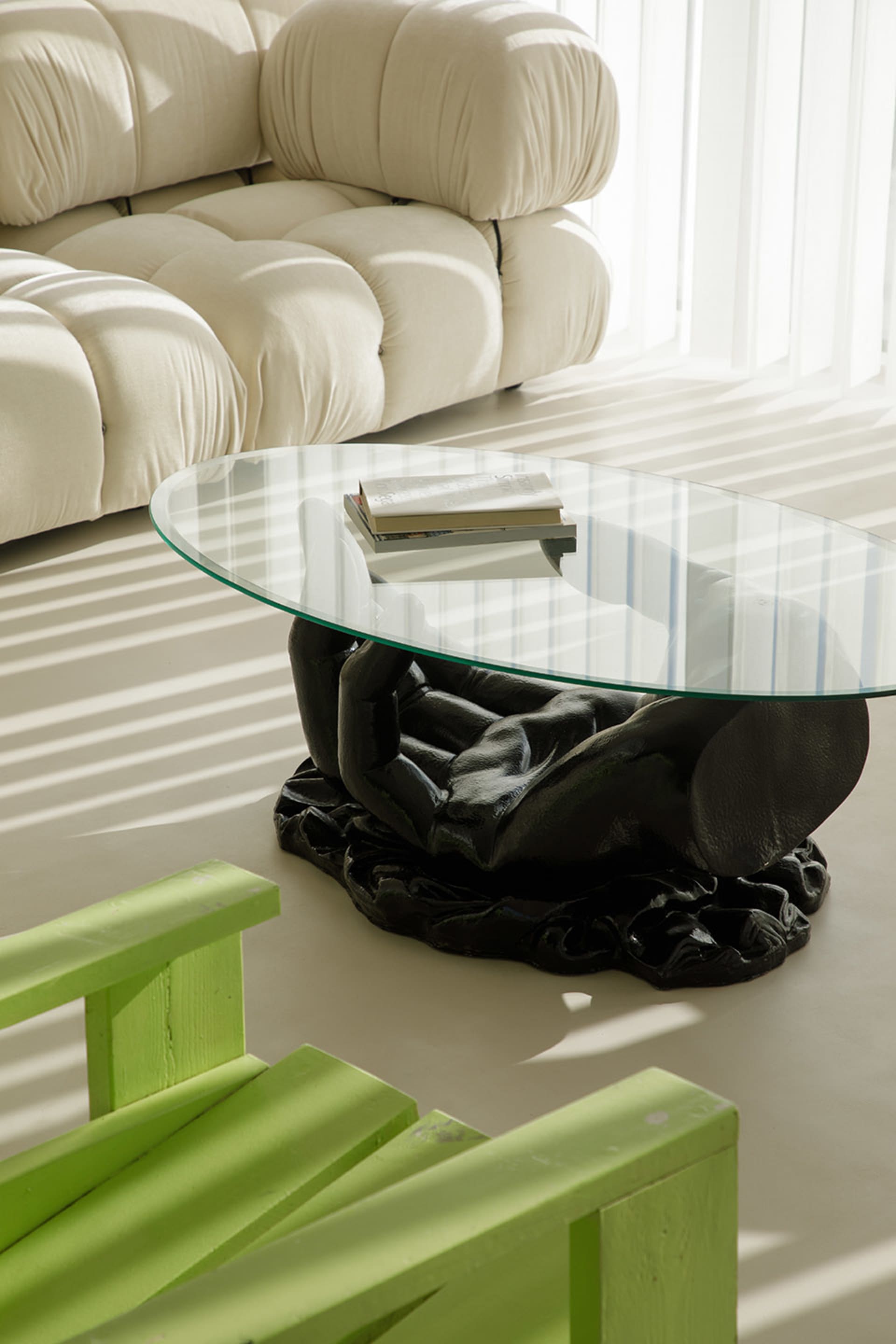 A modern living room featuring a transparent black table and green wooden chairs with sunlight filtering through the window.