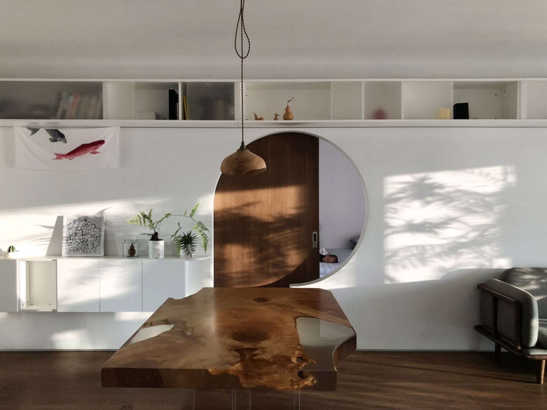 A modern living space features a wooden table with a circular window and natural light.