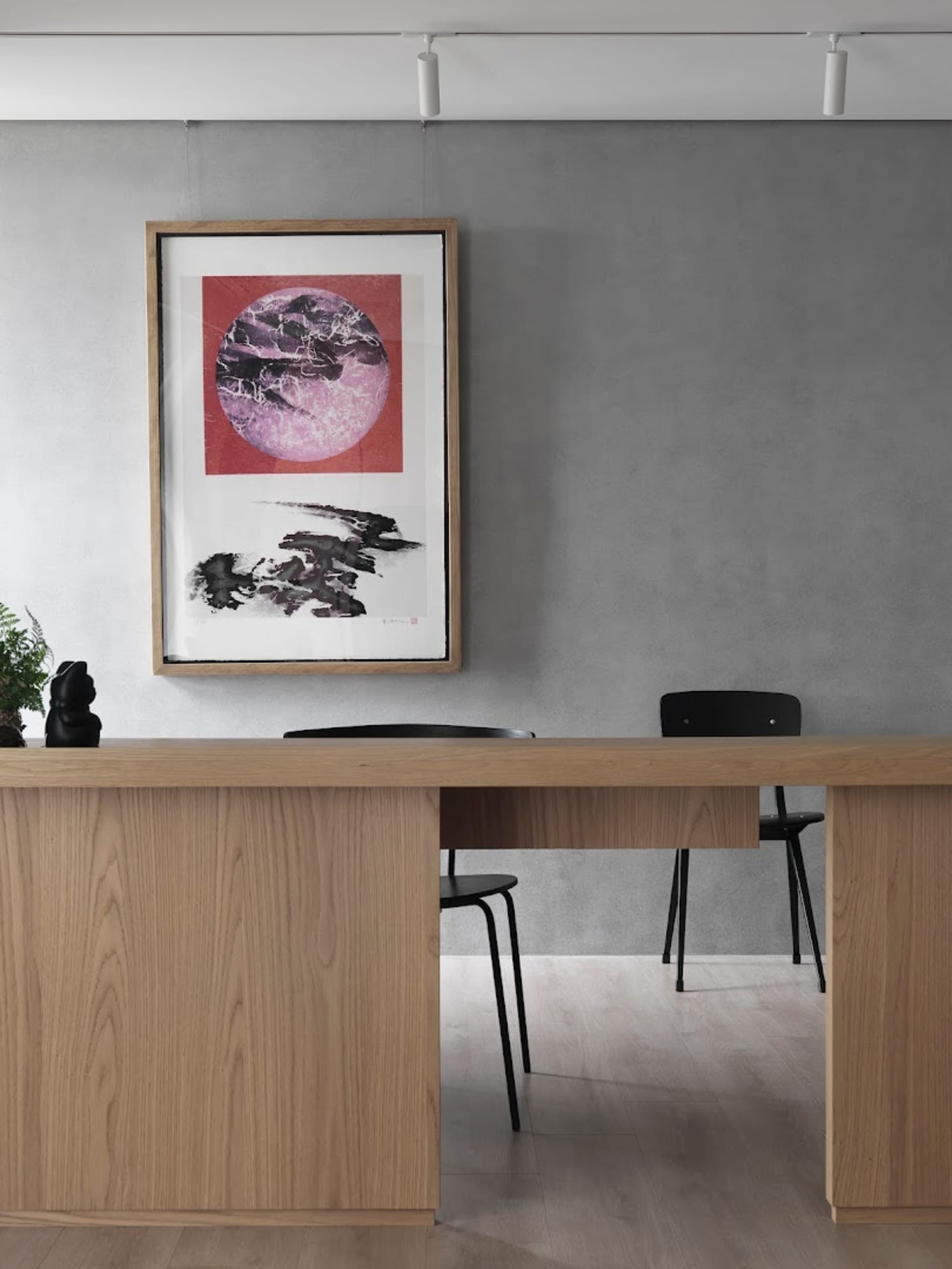 Modern office with a wooden desk and black chair, featuring a framed abstract artwork.
