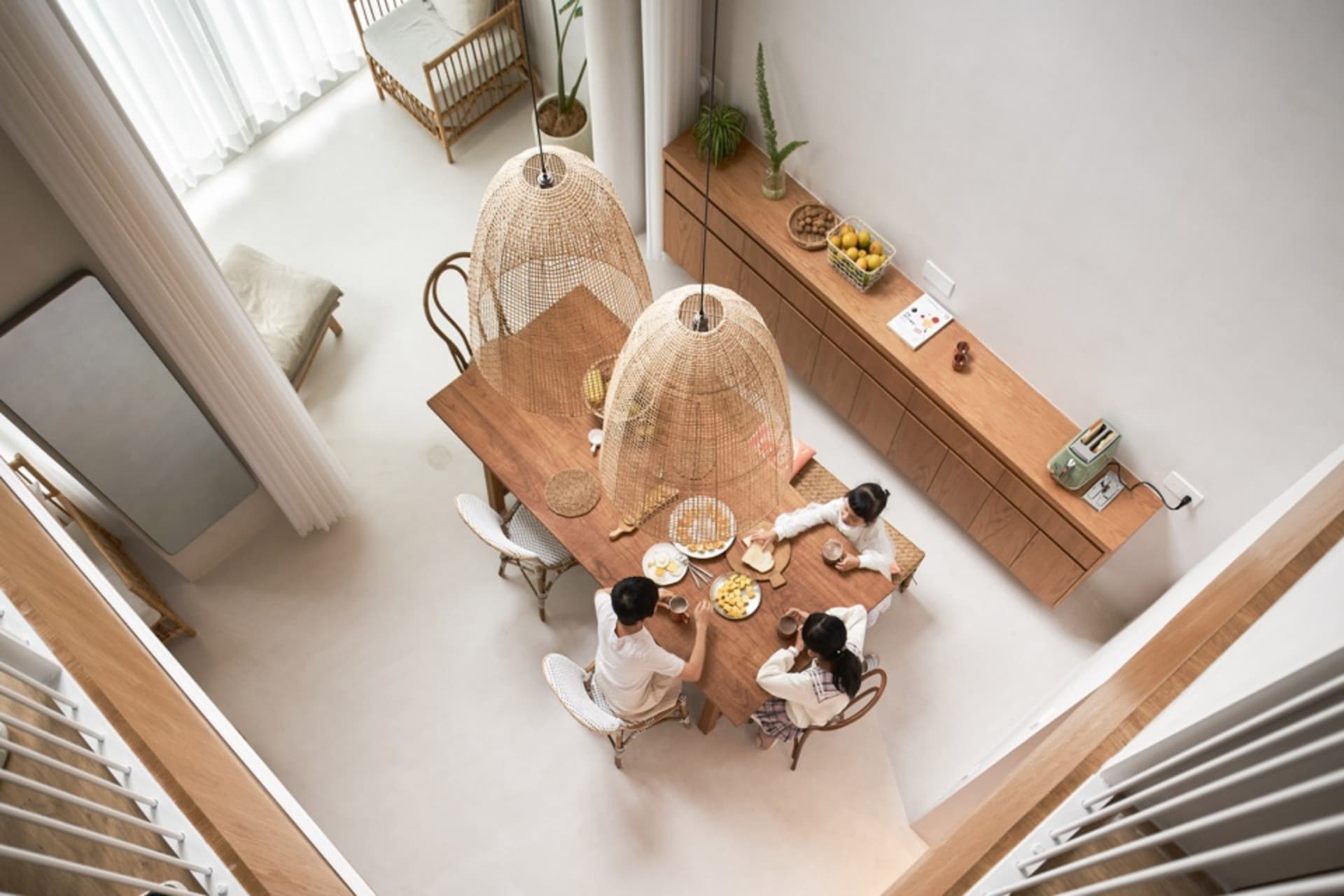 Family gathered together in a modern residential dining room with elegant wood and cane furniture, enjoying a meal with fruit