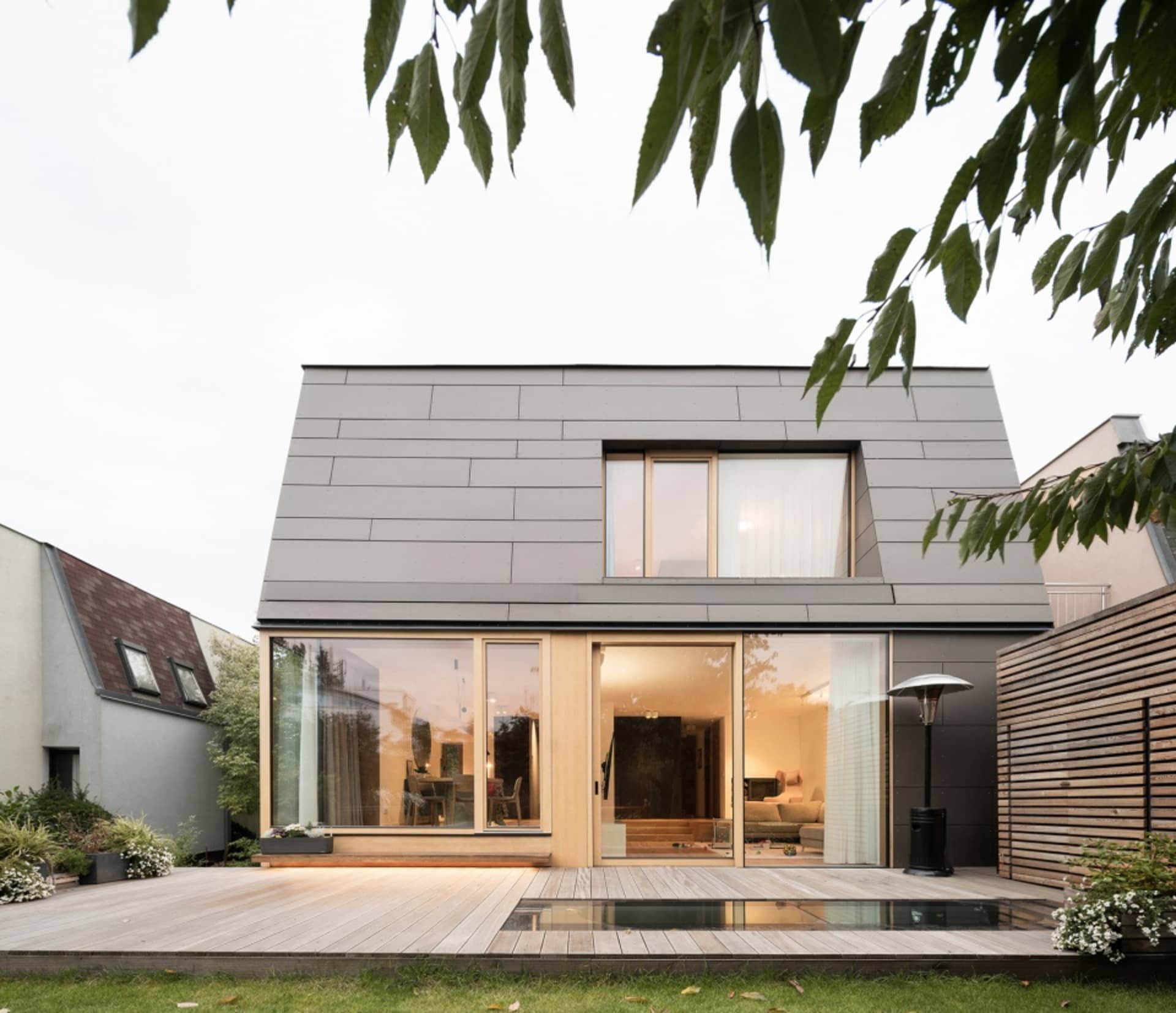 Modern residential house extension featuring wooden deck and glass sliding doors with interior view showing contemporary furn