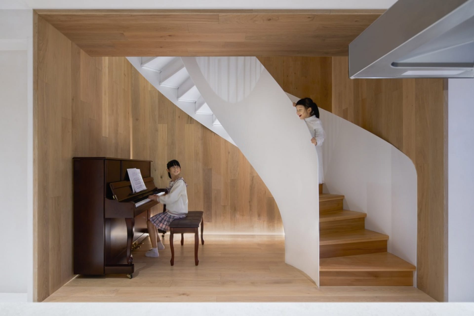 A modern music studio featuring a wooden staircase and a woman playing the piano.