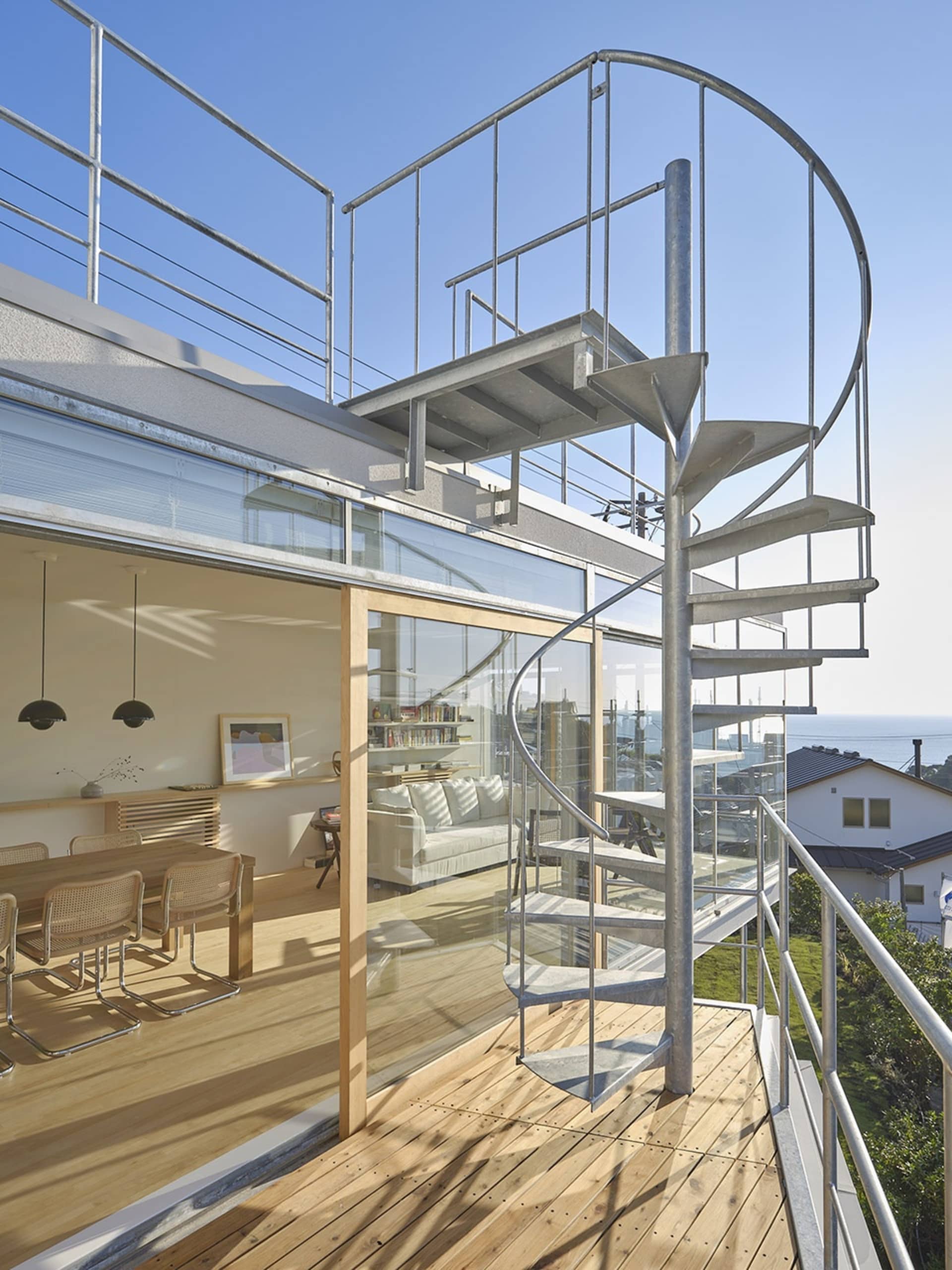 Modern residential home featuring glass, steel, and wood materials, with spiral staircase and outdoor balcony overlooking a c