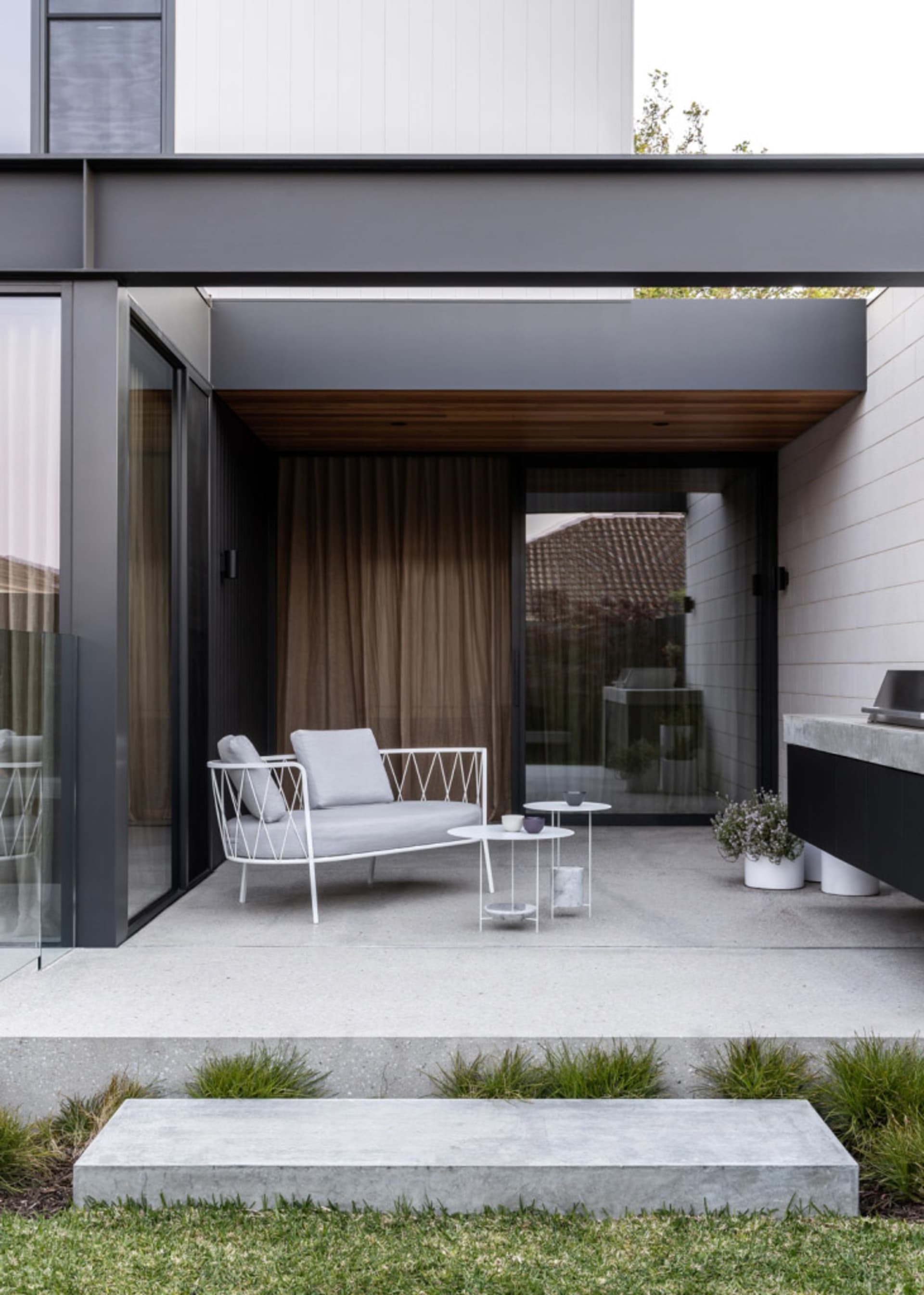 Modern industrial outdoor lounge area featuring a white metal chair with light grey cushions, a metal coffee table, and potte