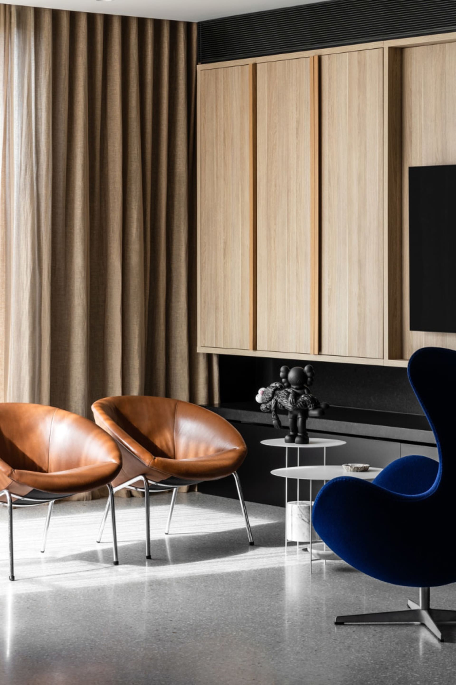 A modern living room featuring two brown leather chairs, a blue upholstered chair, a wooden cabinet, and a black and white sc