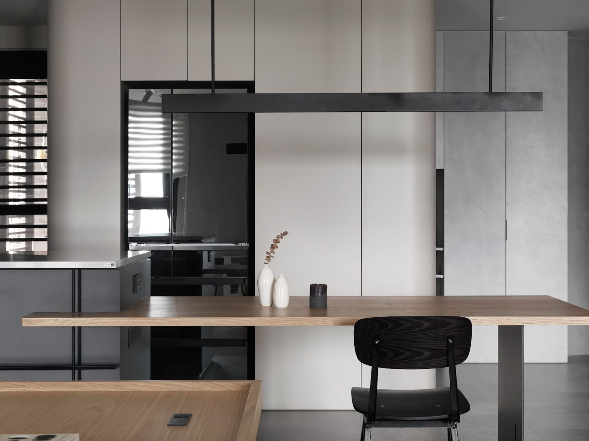 A minimalist modern kitchen with sleek, white cabinets, a wooden dining table, and a black chair.