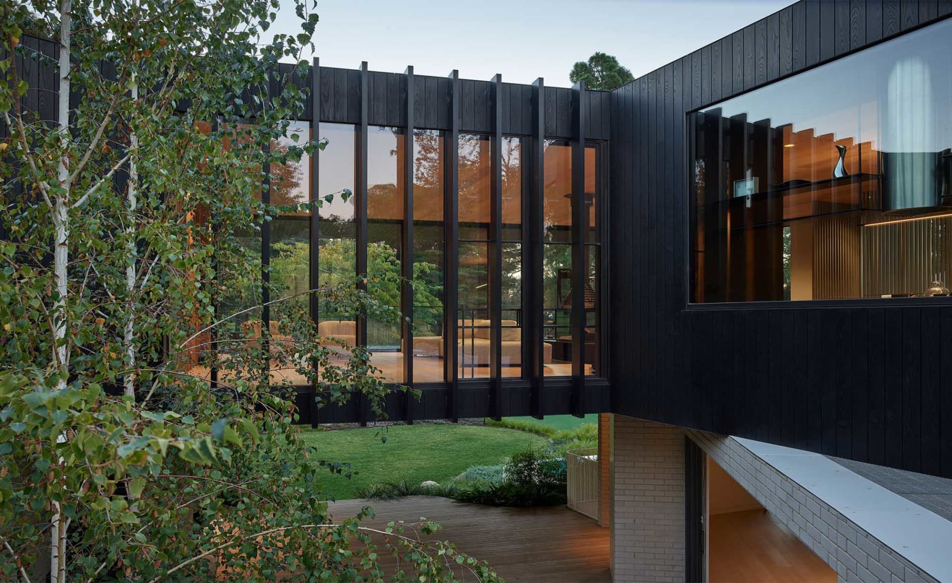 Modern residential exterior with black wood siding and large windows.