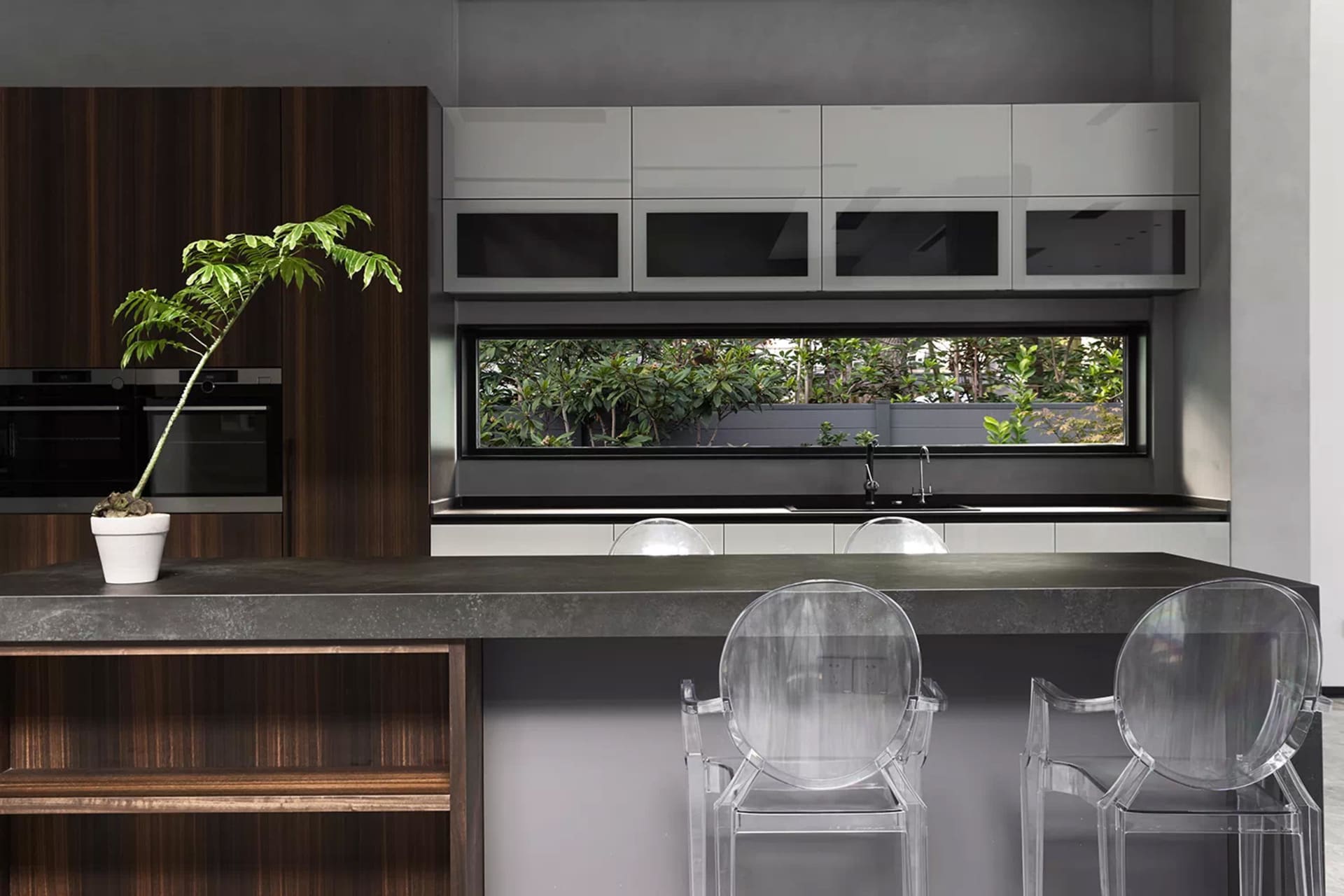 Modern kitchen with concrete countertop, clear plastic chairs, and a potted plant.