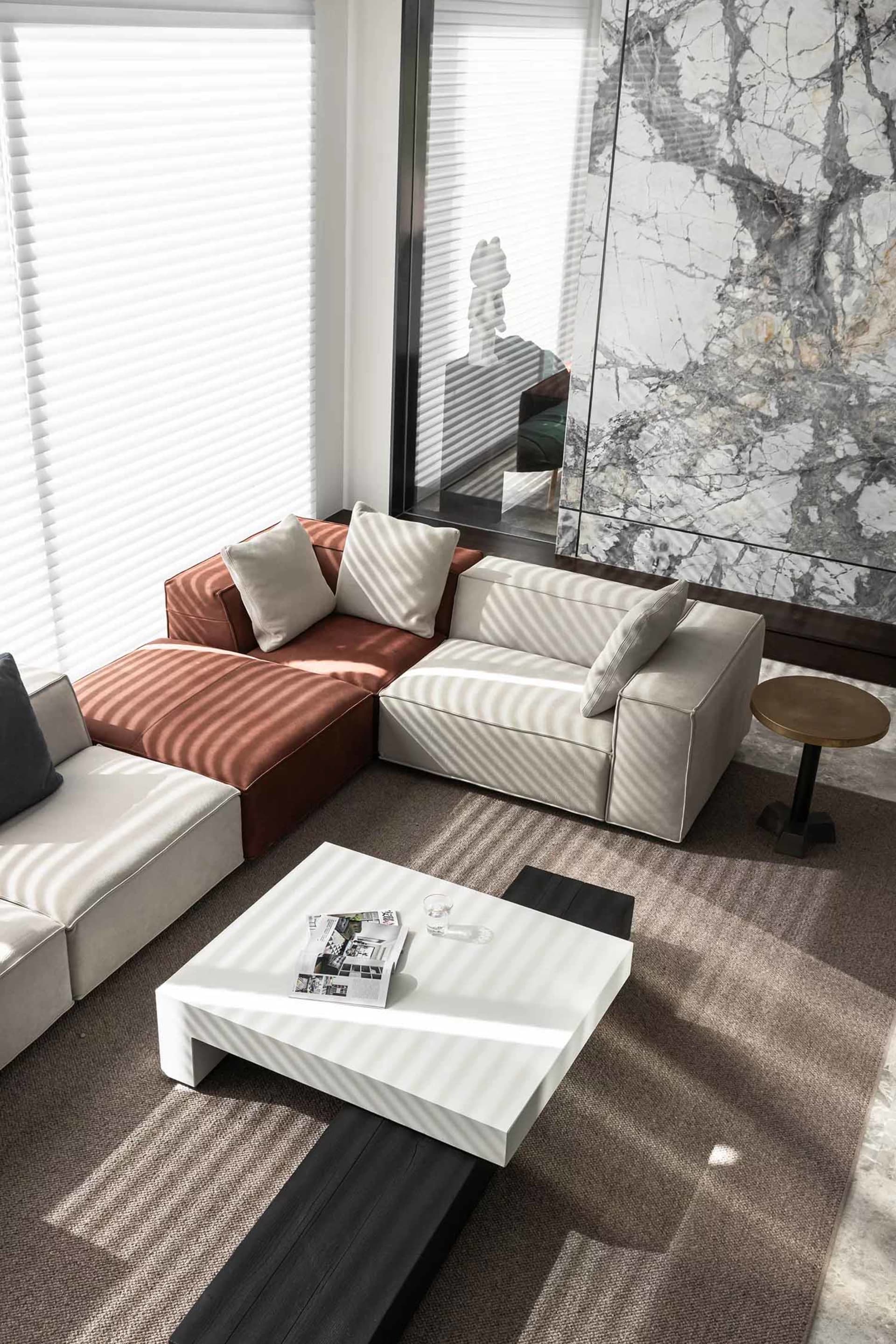 Modern living room with fabric couch, marble accent wall, and floor-to-ceiling windows with blinds.