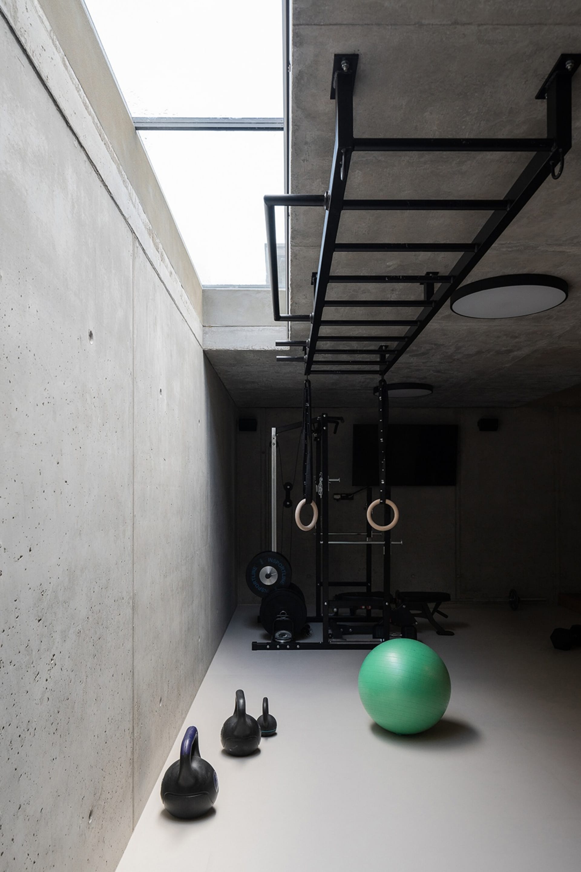 Concrete-walled minimalist gym with exercise equipment and a green exercise ball on the floor.