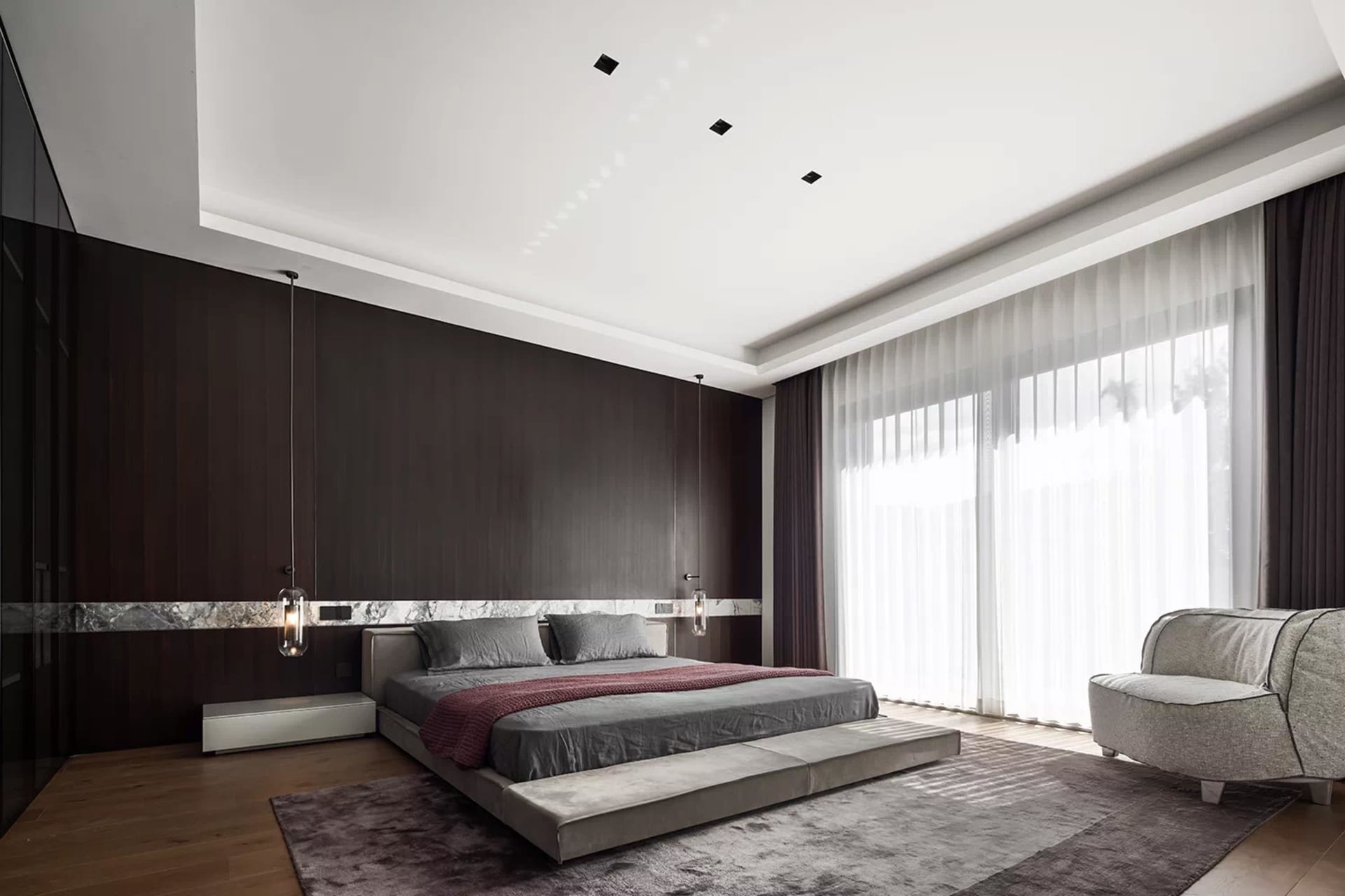 A modern bedroom featuring a dark accent wall, concrete flooring, and a comfortable bed with grey bedding.