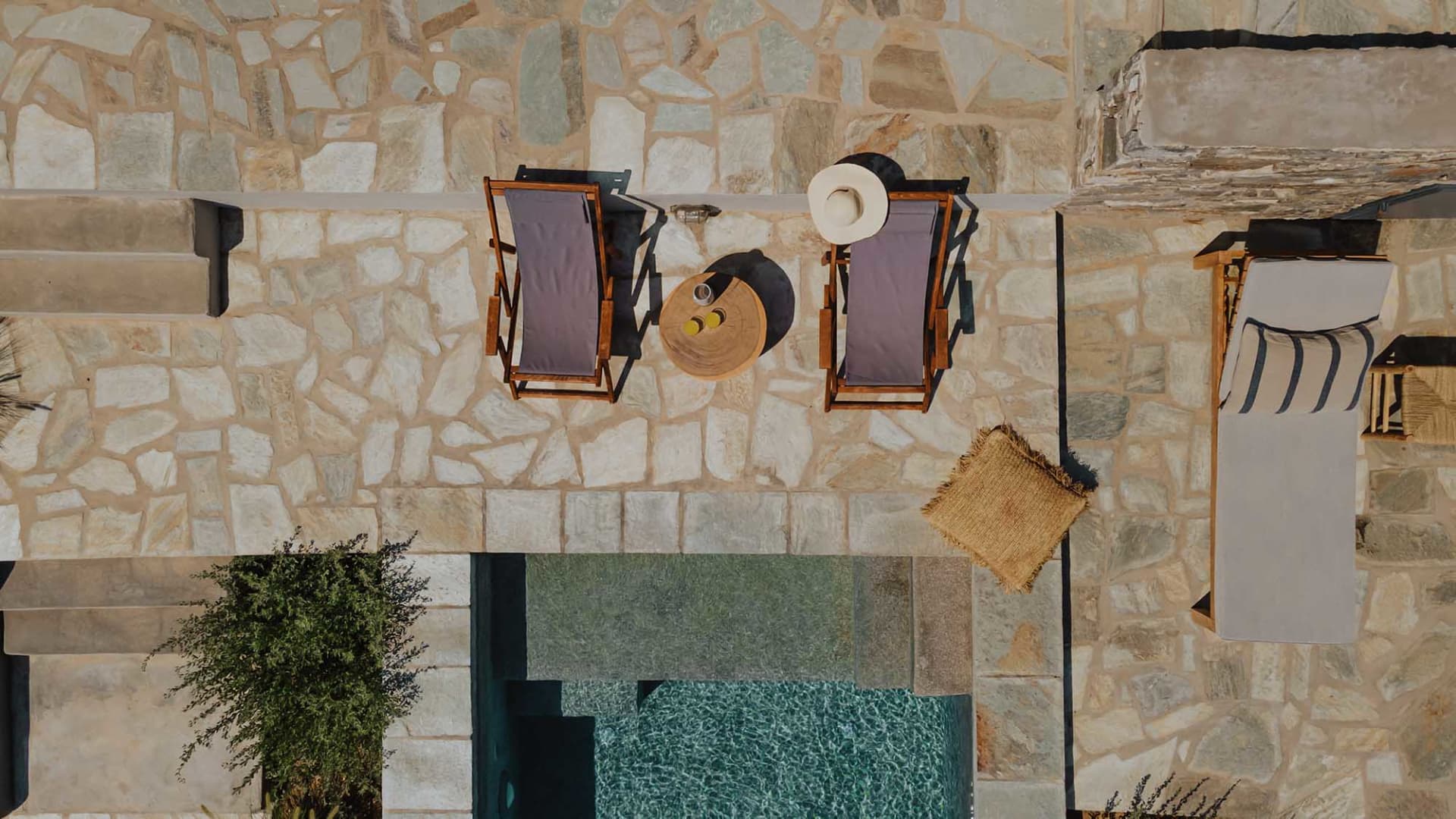 A stone-paved seating area with a table and chairs next to a pool.