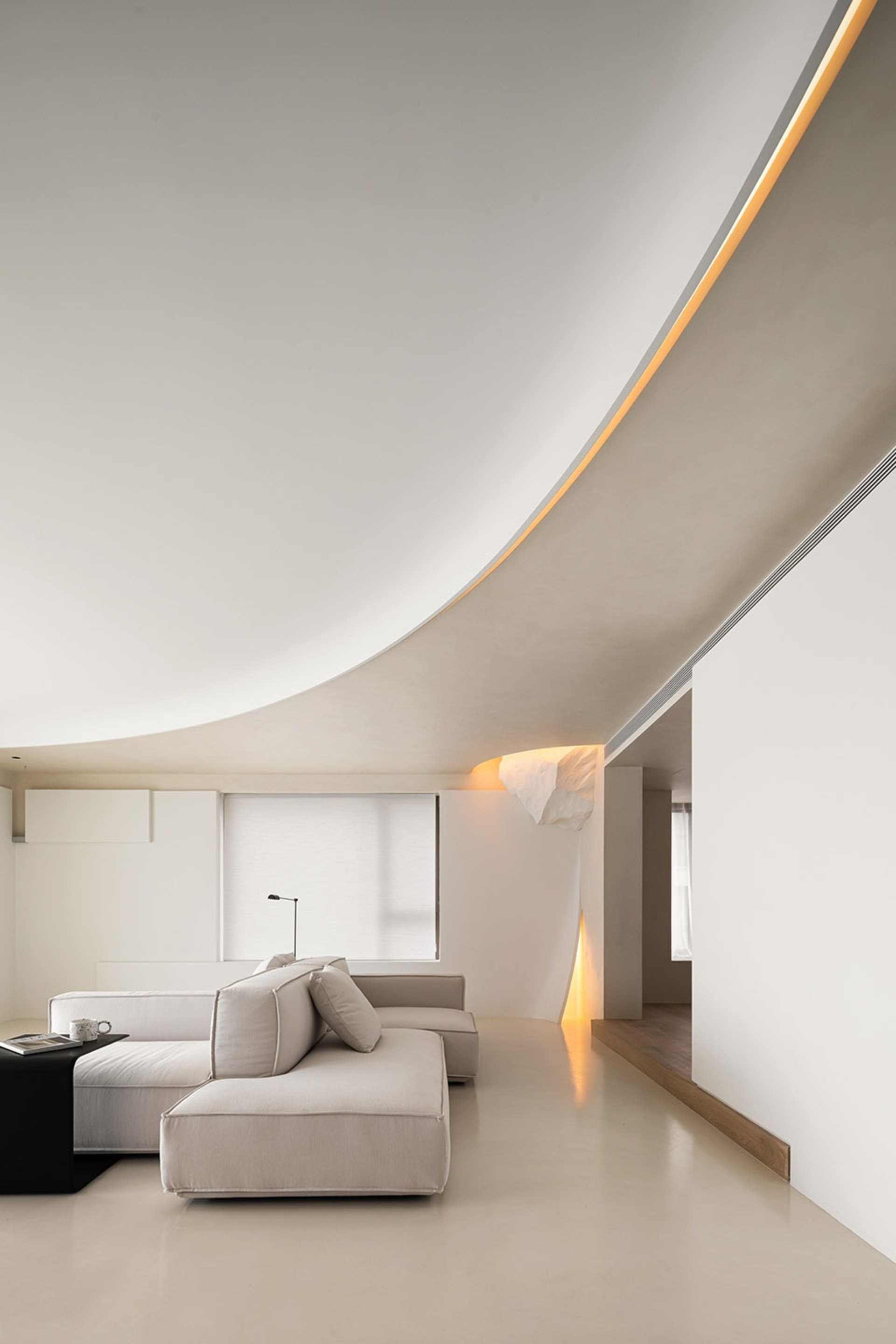 Modern minimalist living room with concrete walls and floor, featuring a white sectional sofa and a sleek, low-profile coffee